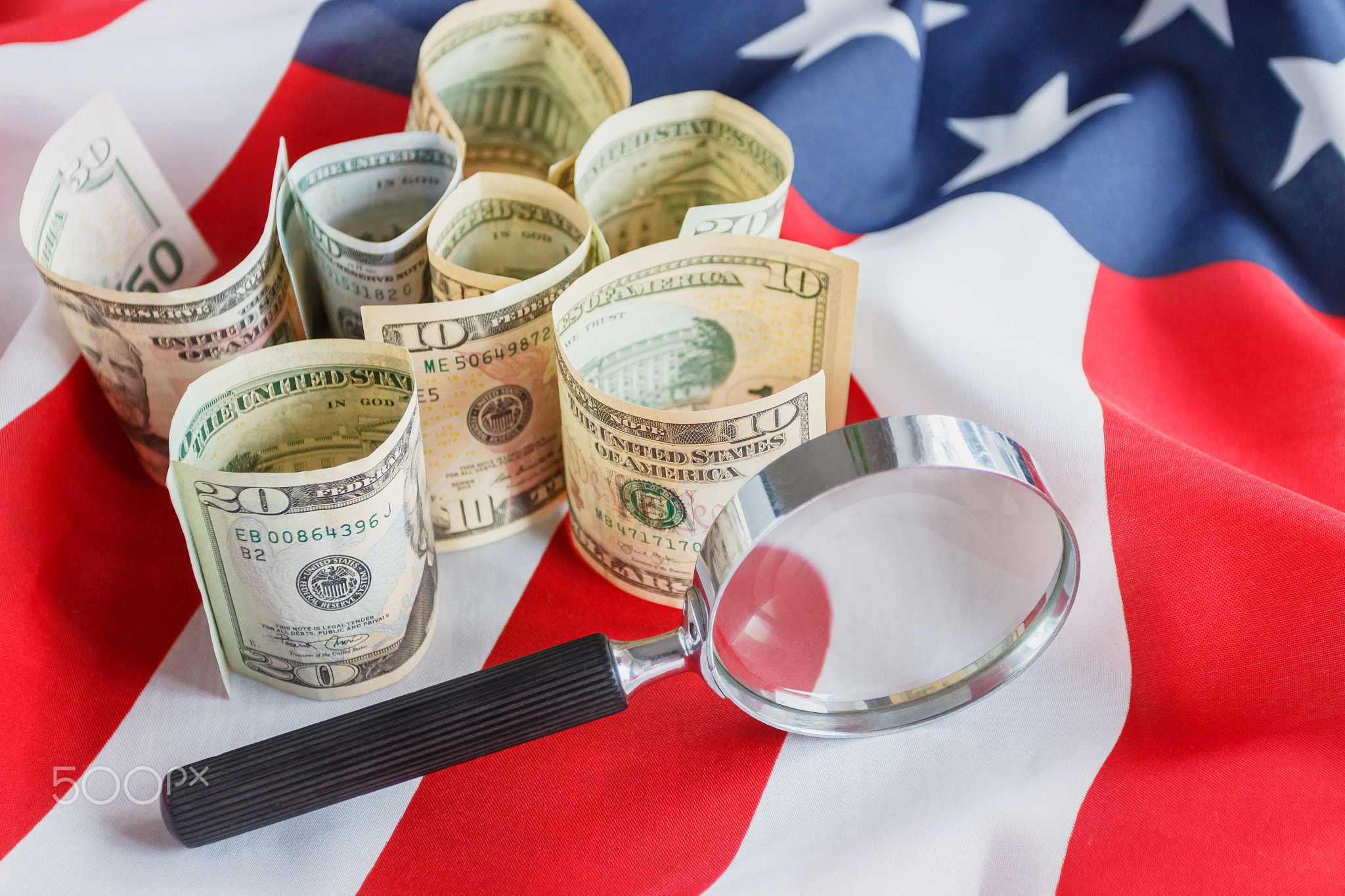 Magnifying glass and American dollars on the national flag of United States of America, background