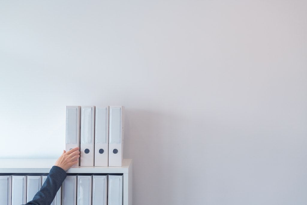 Hand reaching for document ring binder on office shelf by Igor Stevanovic on 500px.com