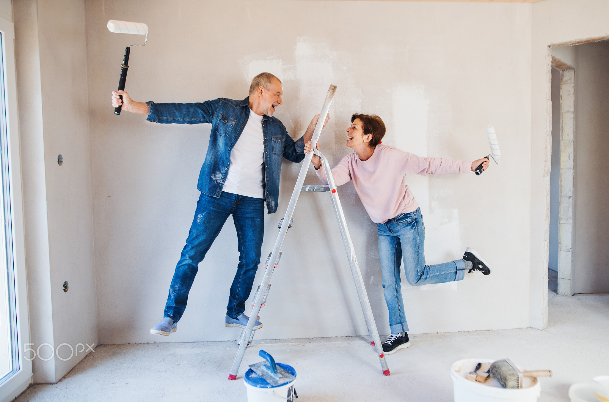 Senior couple painting walls in new home, having fun. Relocation concept.