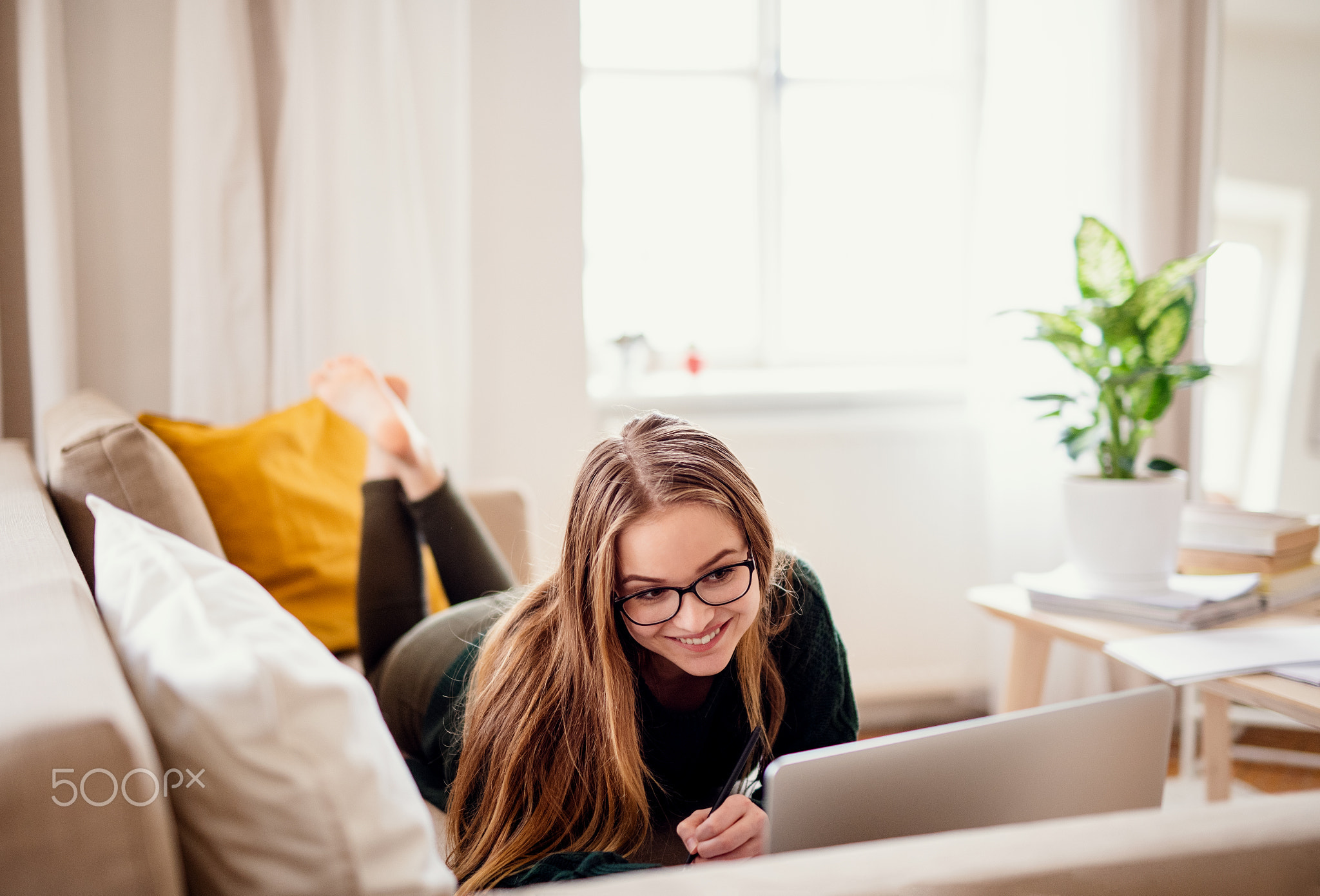 A young female student lying on sofa, using laptop when studying.