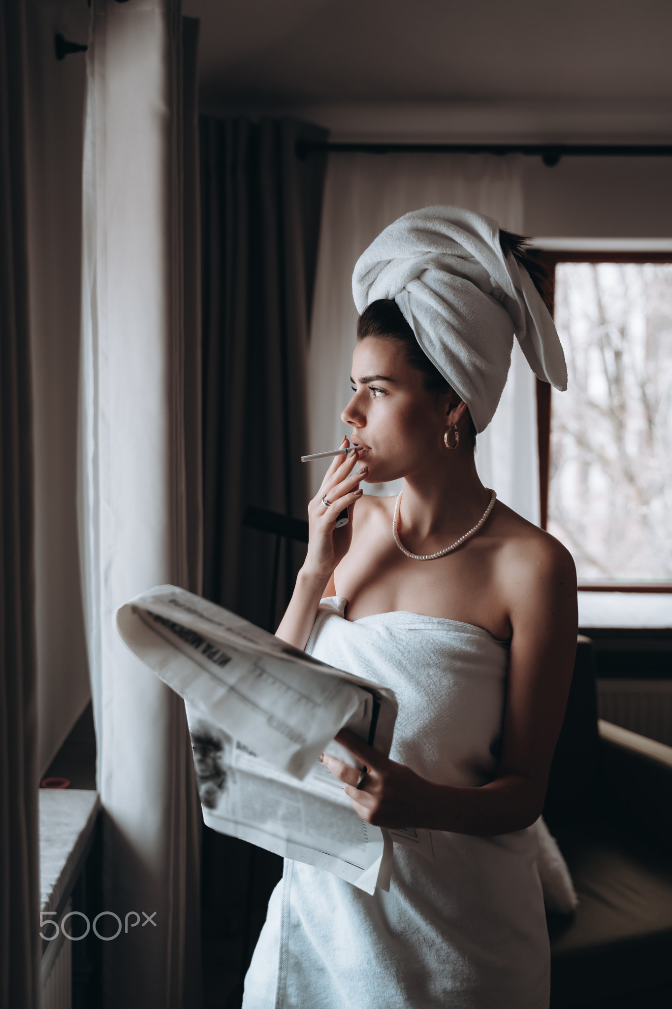 Beautiful young woman in a towel smokes a cigarette and reads newspaper