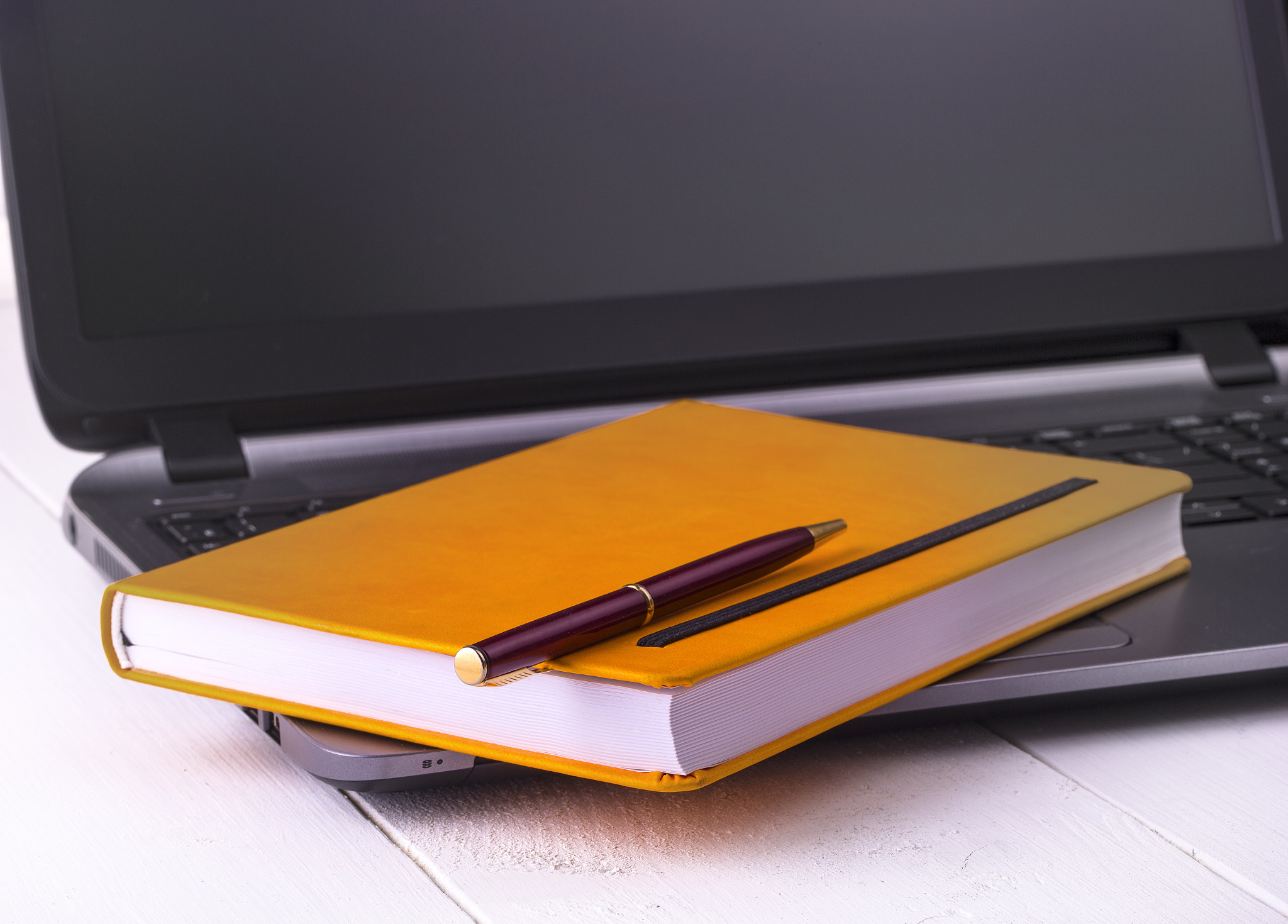 Orange notebook with a pencil lying on a laptop