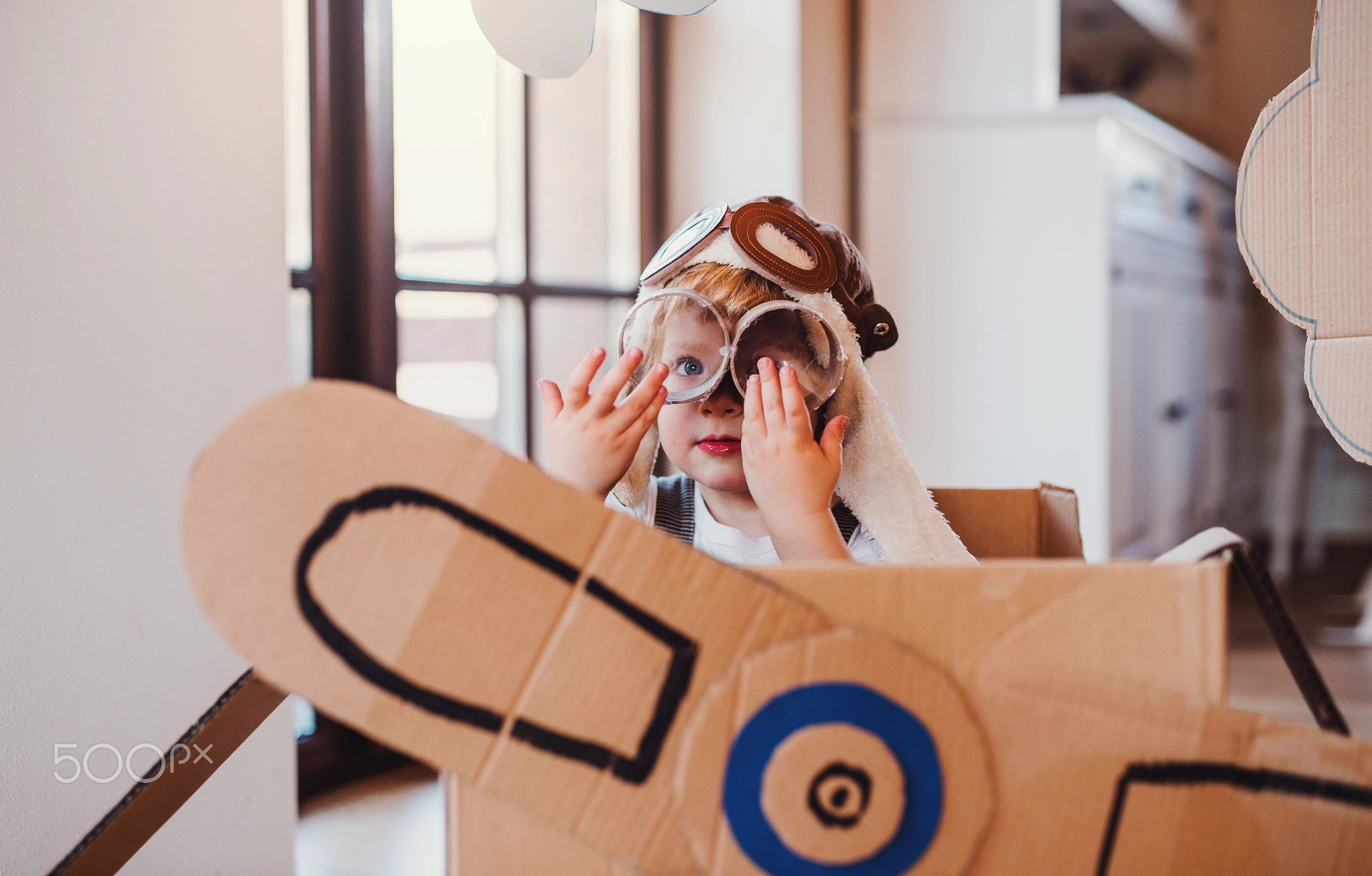 A toddler boy with carton plane playing indoors at home, flying concept.