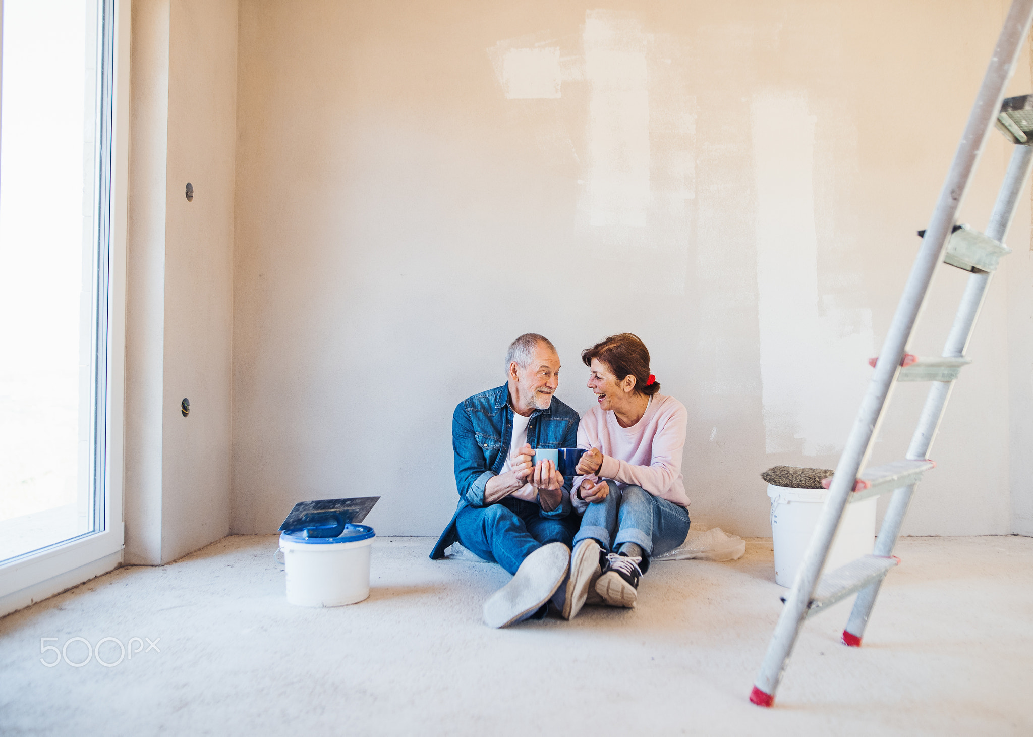 Senior couple painting walls in new home, resting. Relocation concept.