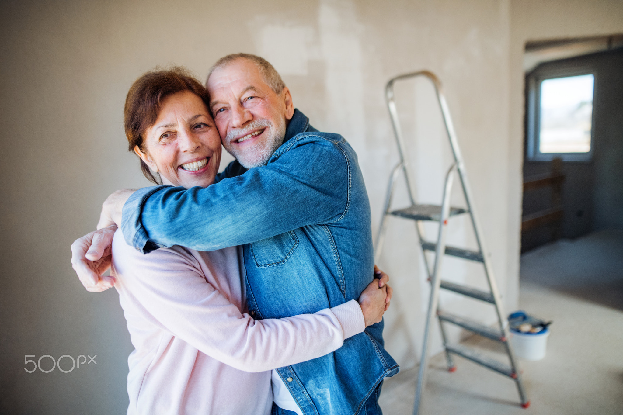 Senior couple painting walls in new home, hugging. Relocation concept.