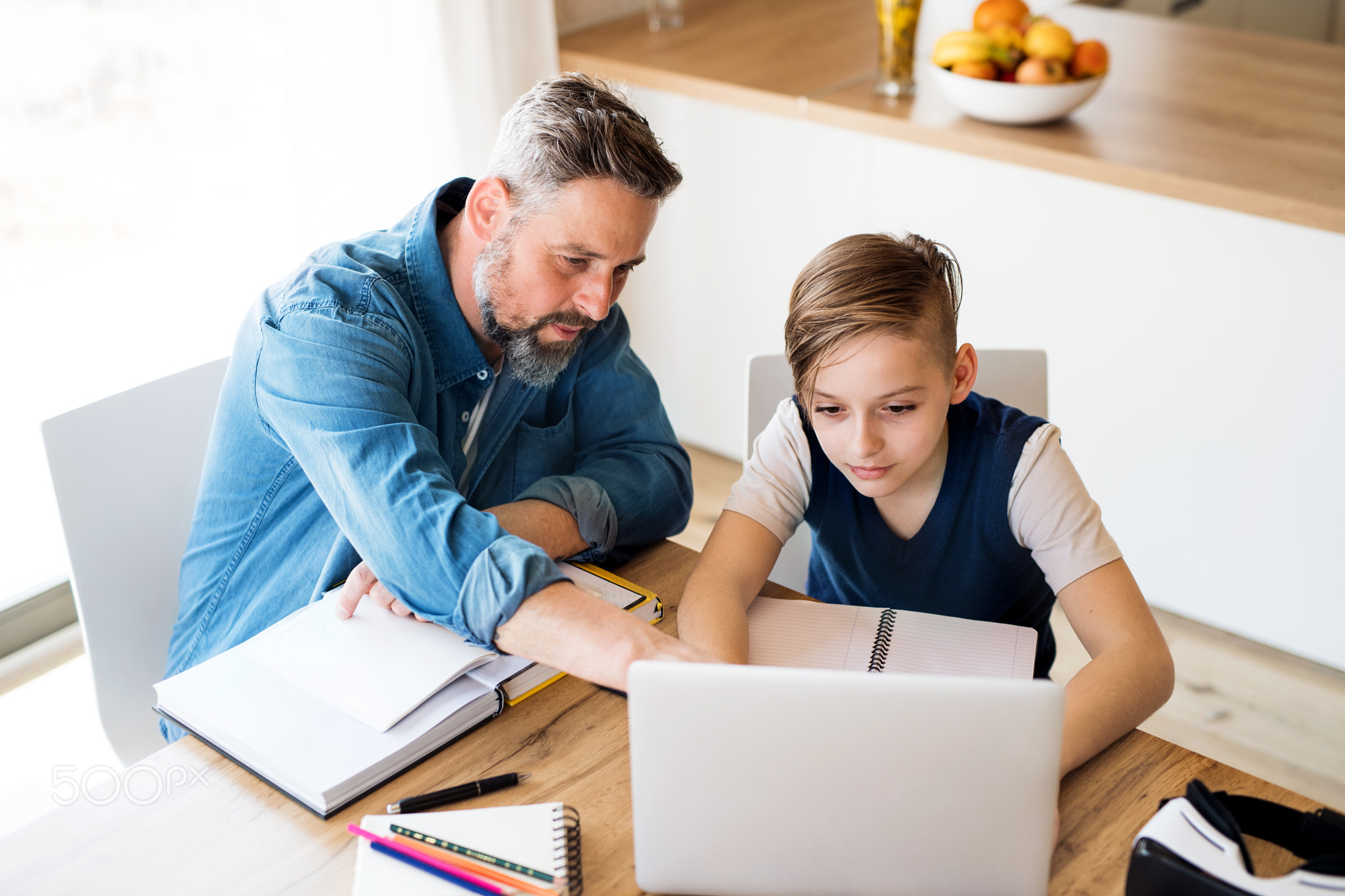 Mature father with small son sitting at table indoors, using laptop.