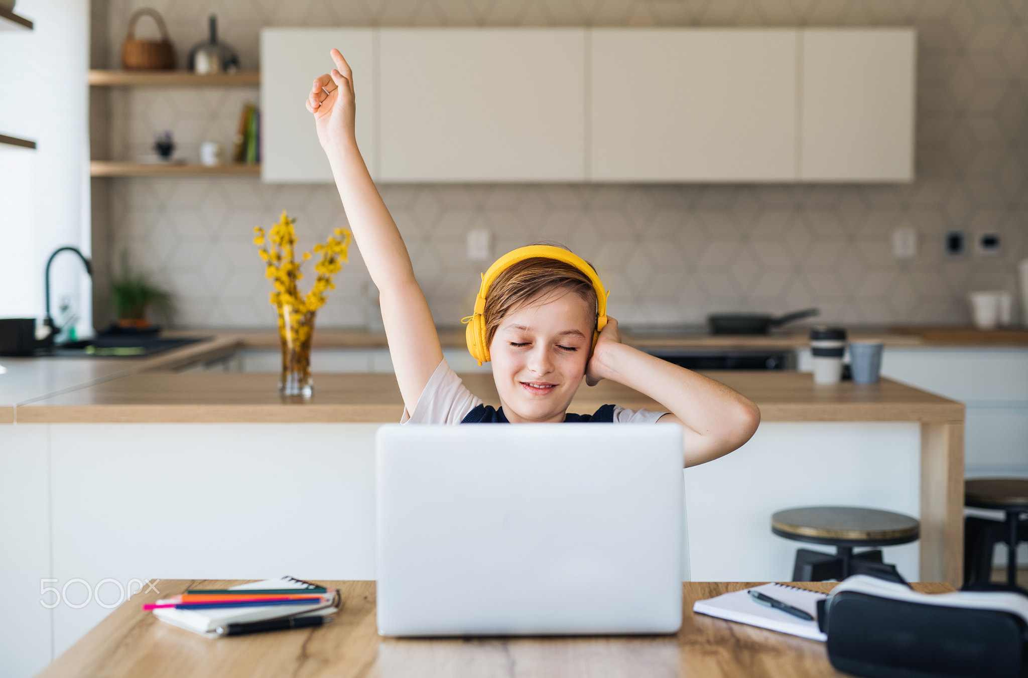 Small boy with headphones and laptop sitting at the table indoors at home.
