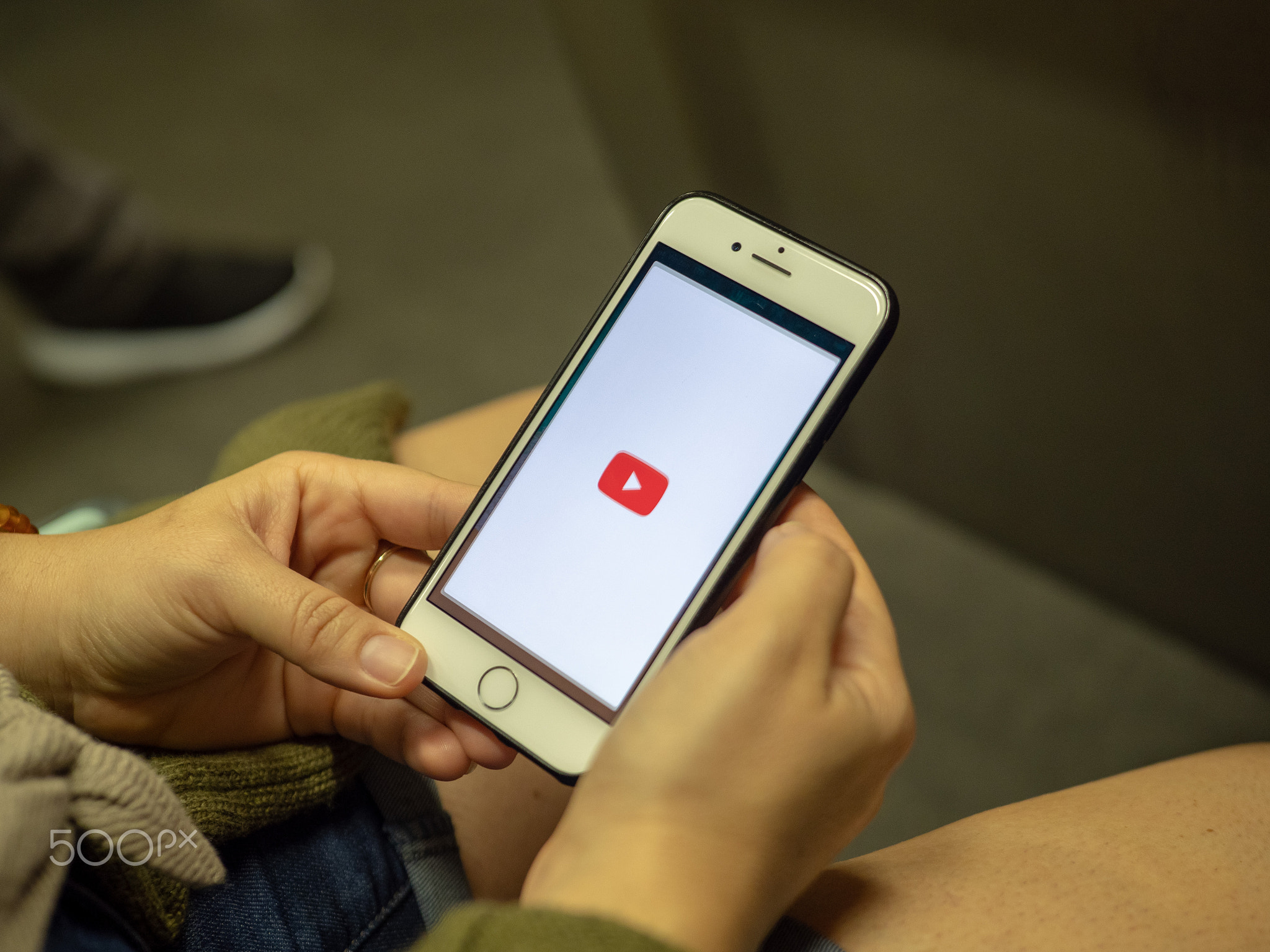 Woman opening YouTube mobile app with logo on iPhone screen while commuting on subway train