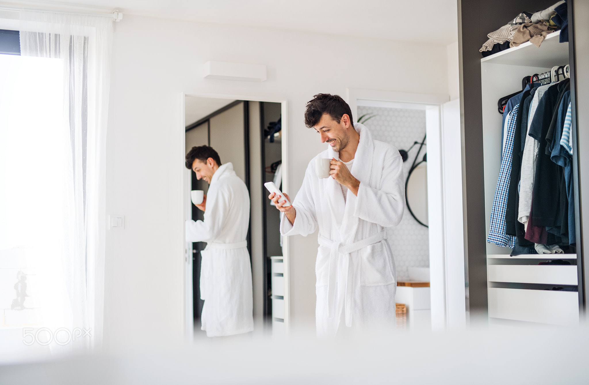 Young man with coffee and smartphone in the bedroom, a morning routine.