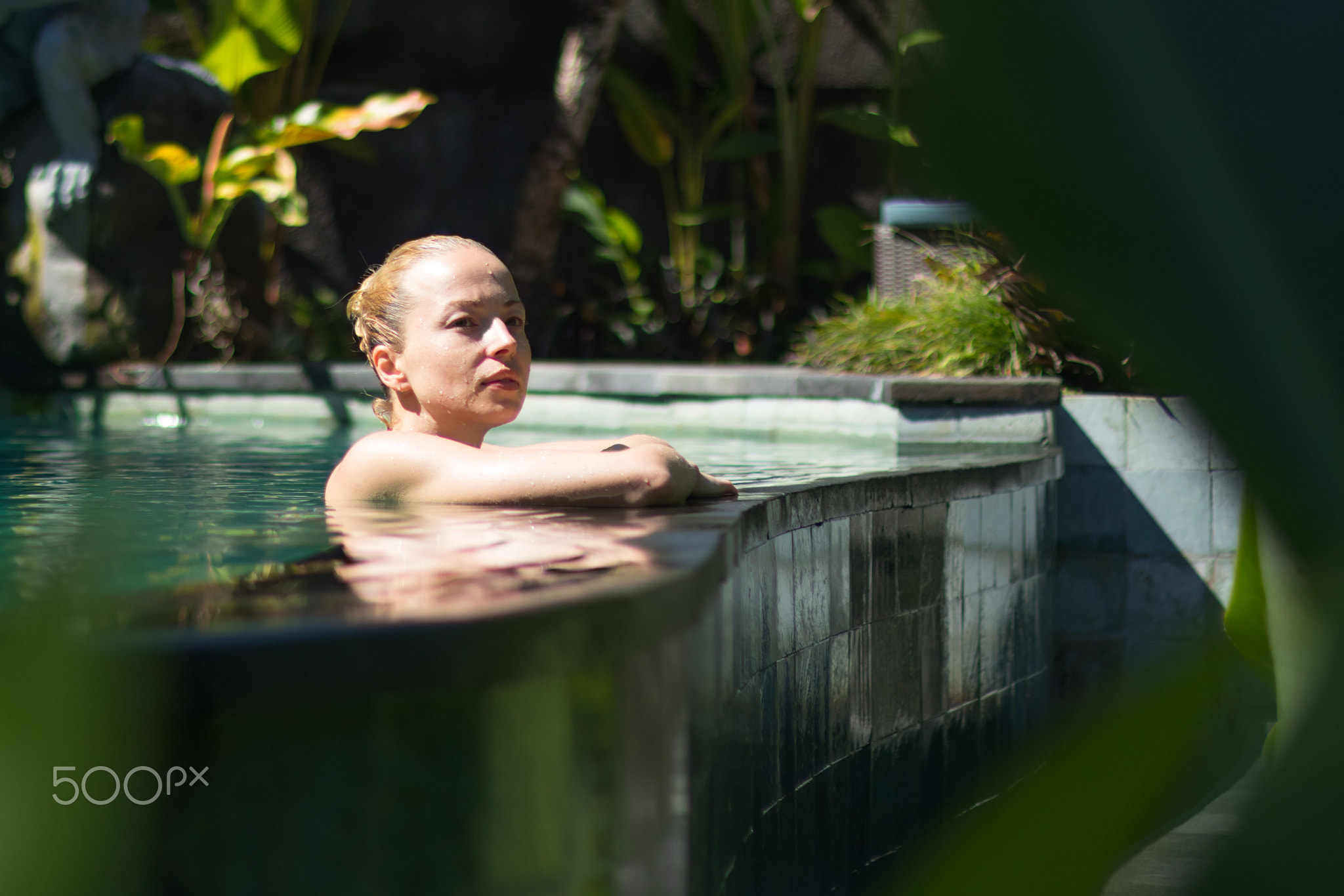 Sensual young woman relaxing in outdoor spa infinity swimming pool surrounded with lush tropical...