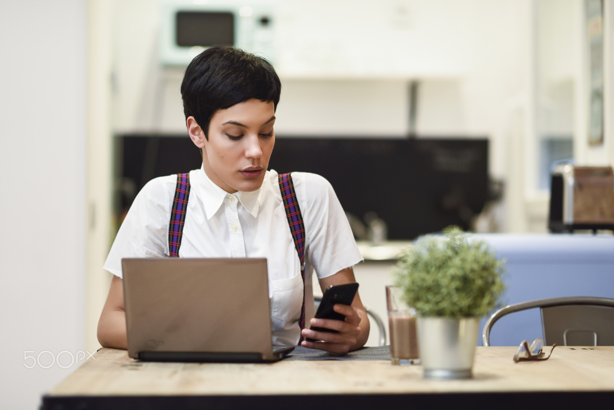Young businesswoman with very short haircut looking at her smartphone at home.