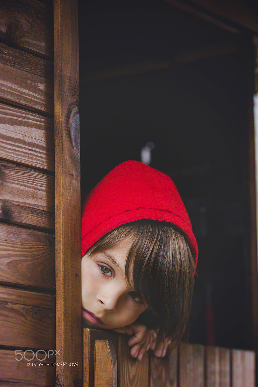 Preteen boy in red sweatshirt, hiding behind a wooden door, look