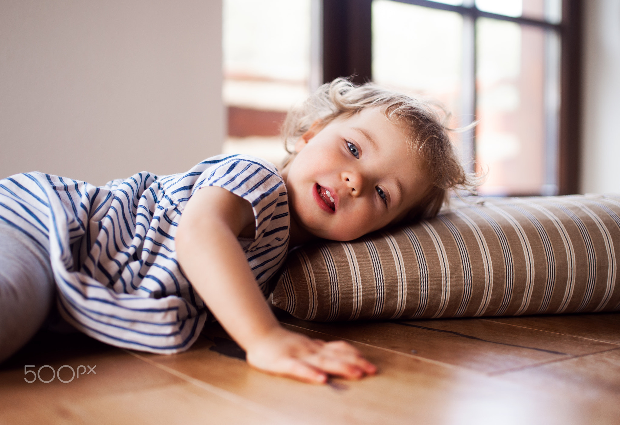 A toddler girl lying on the floor indoors at home, playing.