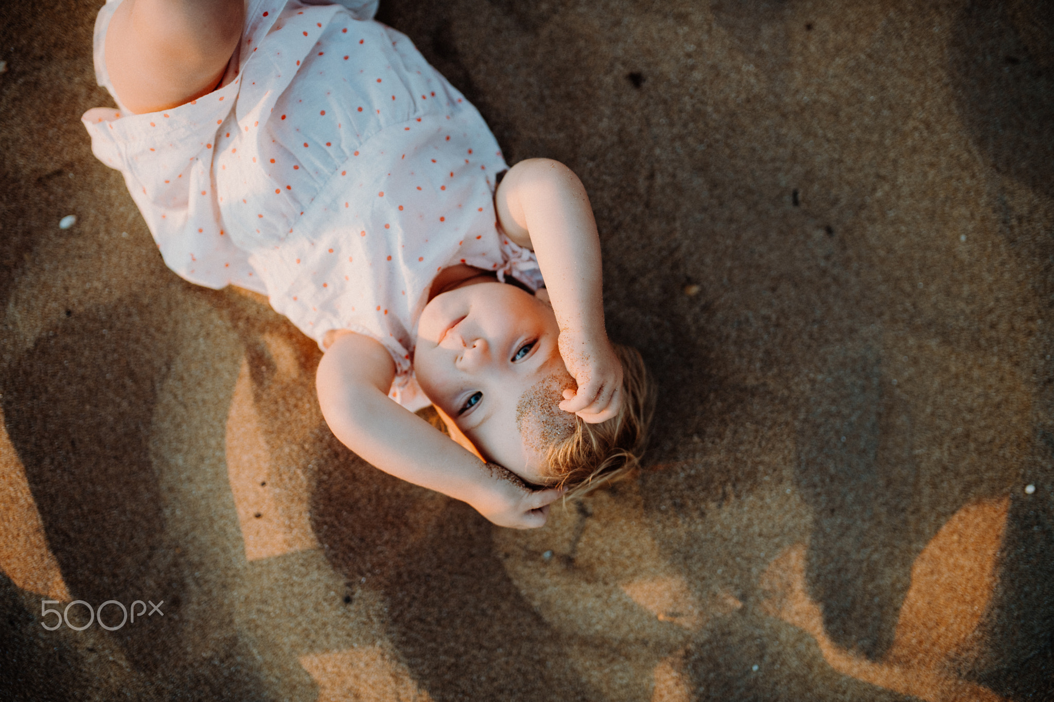 A top view of small toddler girl playing in sand on beach on summer holiday.