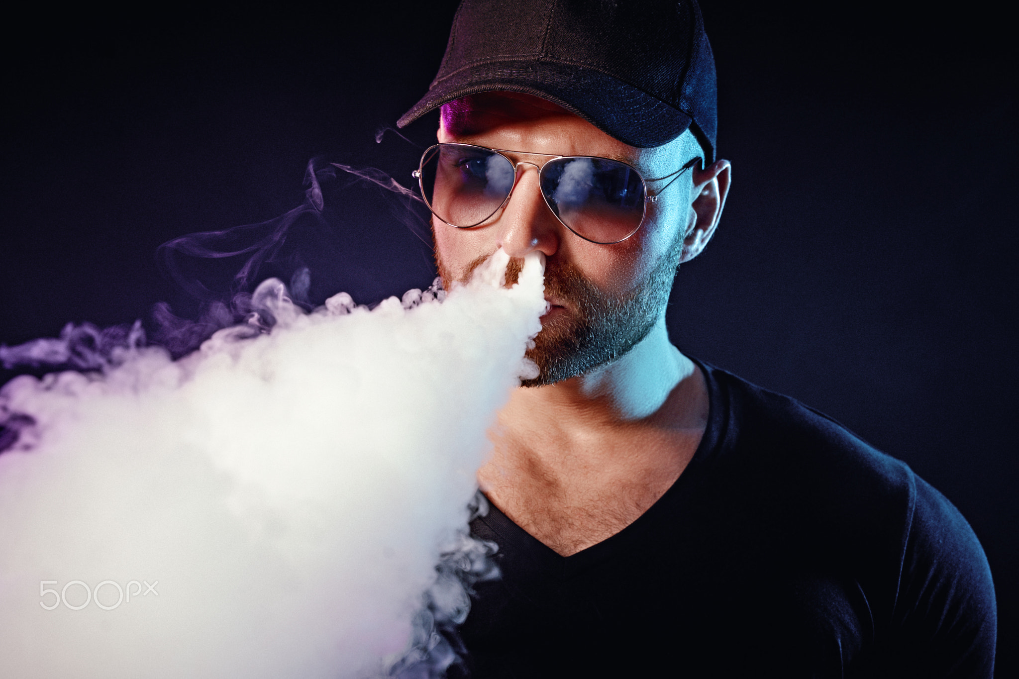 Men with beard in sunglasses vaping and releases a cloud of vapor
