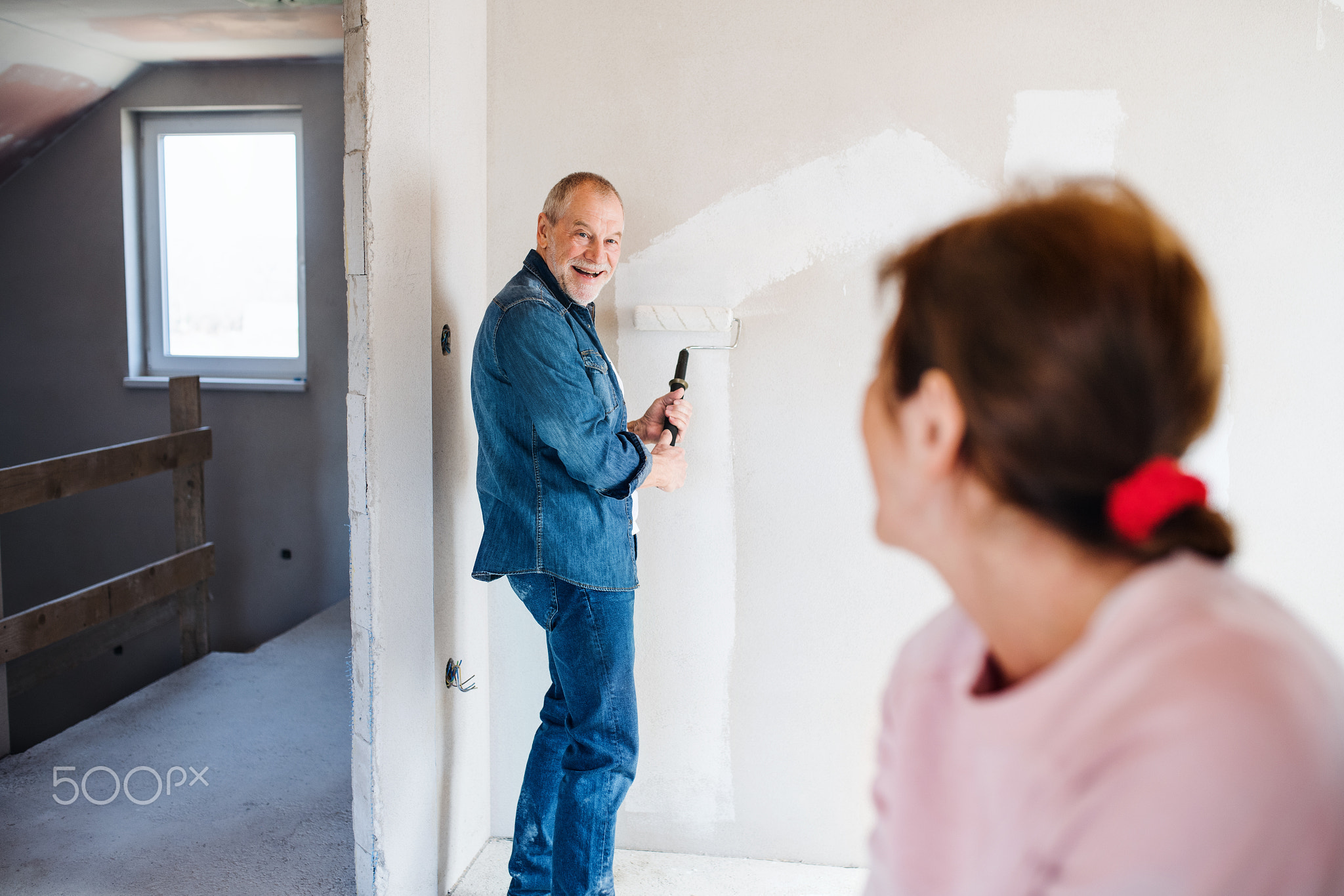 Senior couple painting walls in new home, relocation concept.