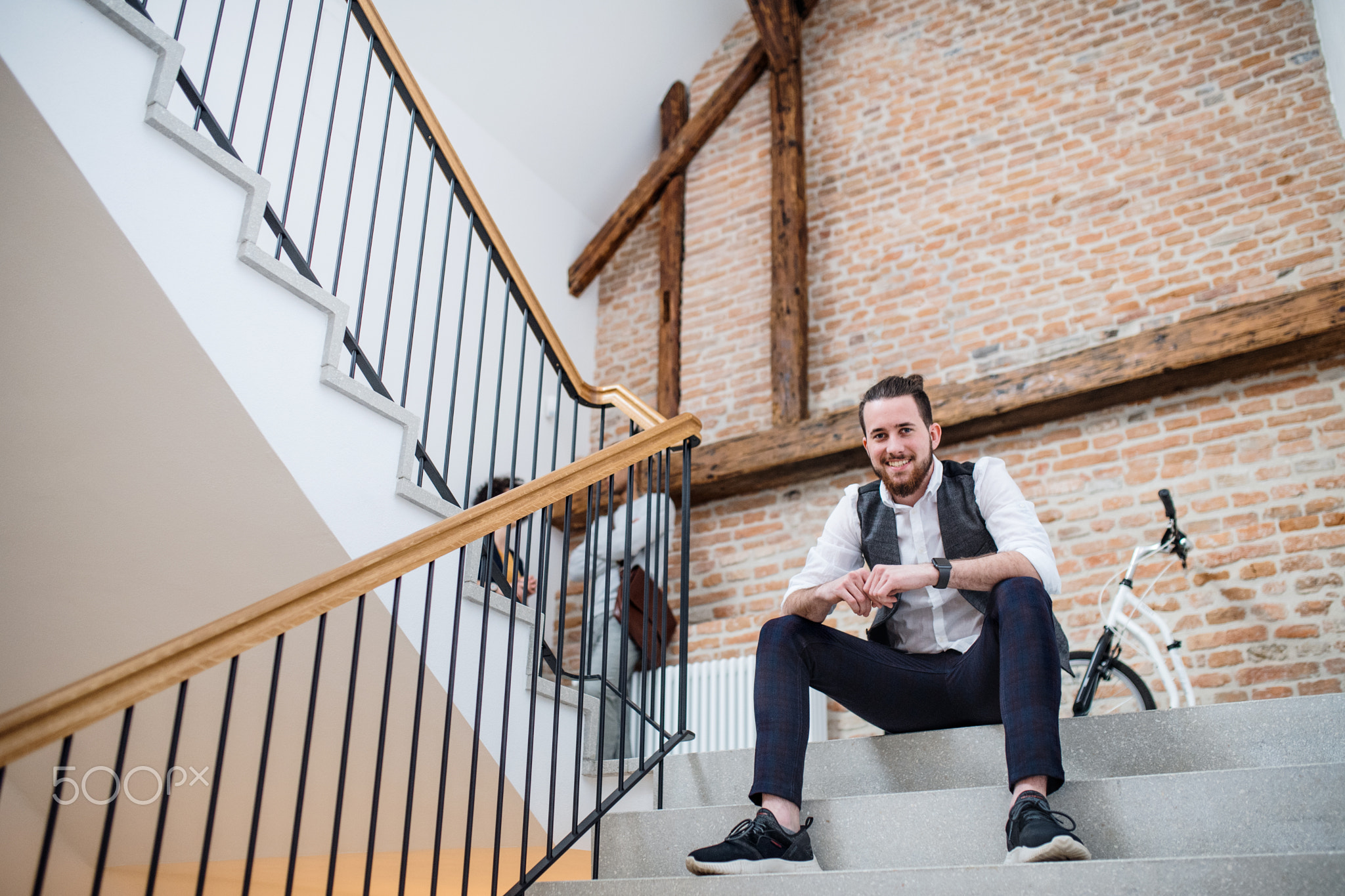 Young businessman sitting on stairs in office building, looking at camera.