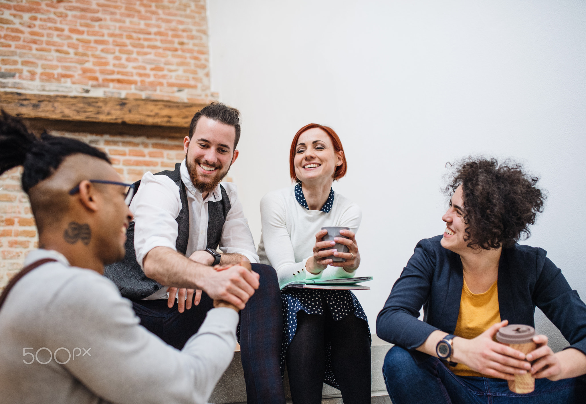 Group of young businesspeople sitting on stairs in indoors, talking.