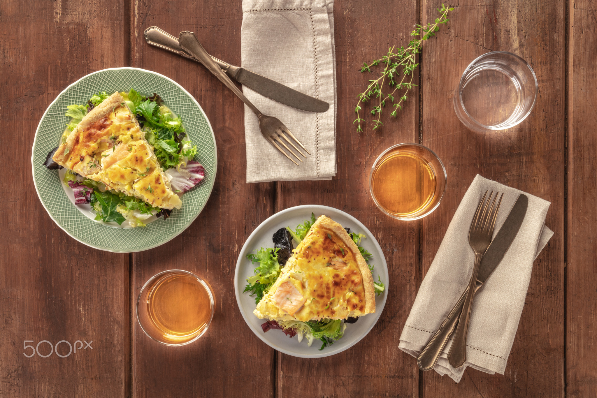 Slices of a French quiche with salmon, with green salad leaves, thyme and white wine, shot from...