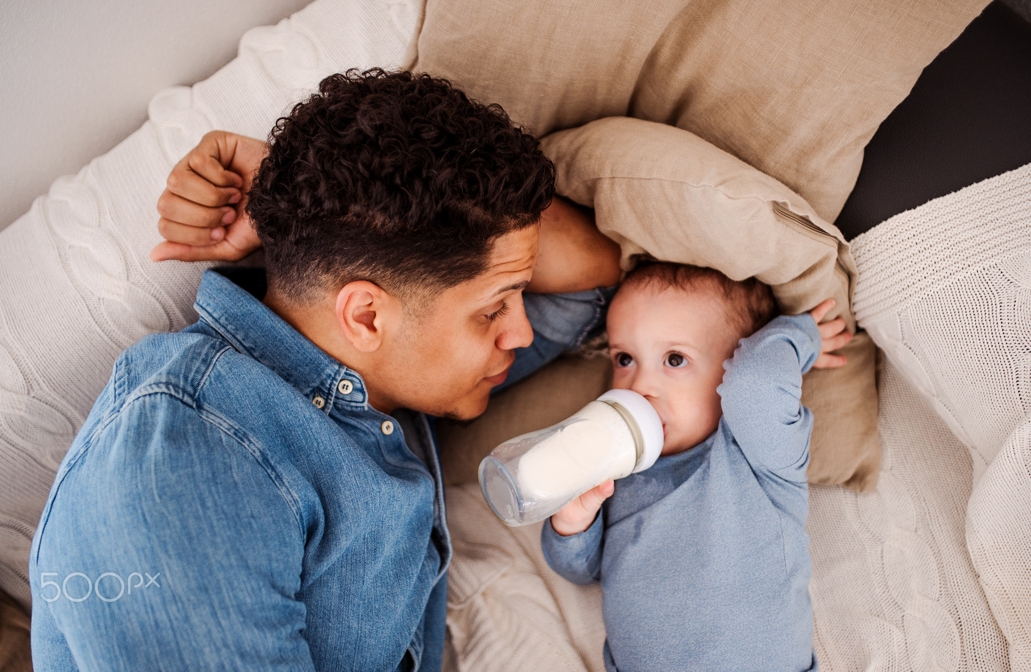 A top view of father and a son indoors at home, drinking milk from bottle.