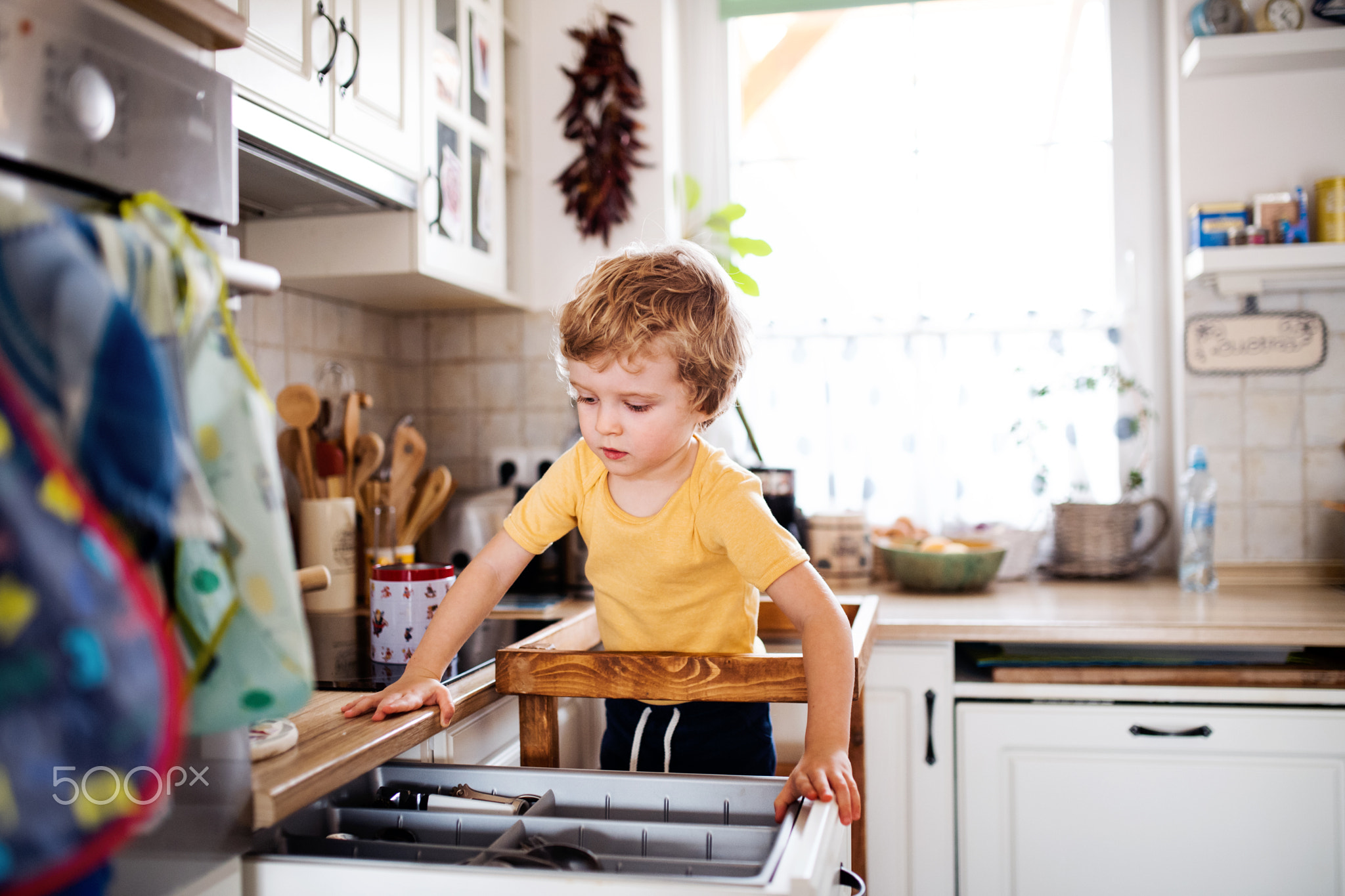 A small toddler boy standing in a kitchen at home.