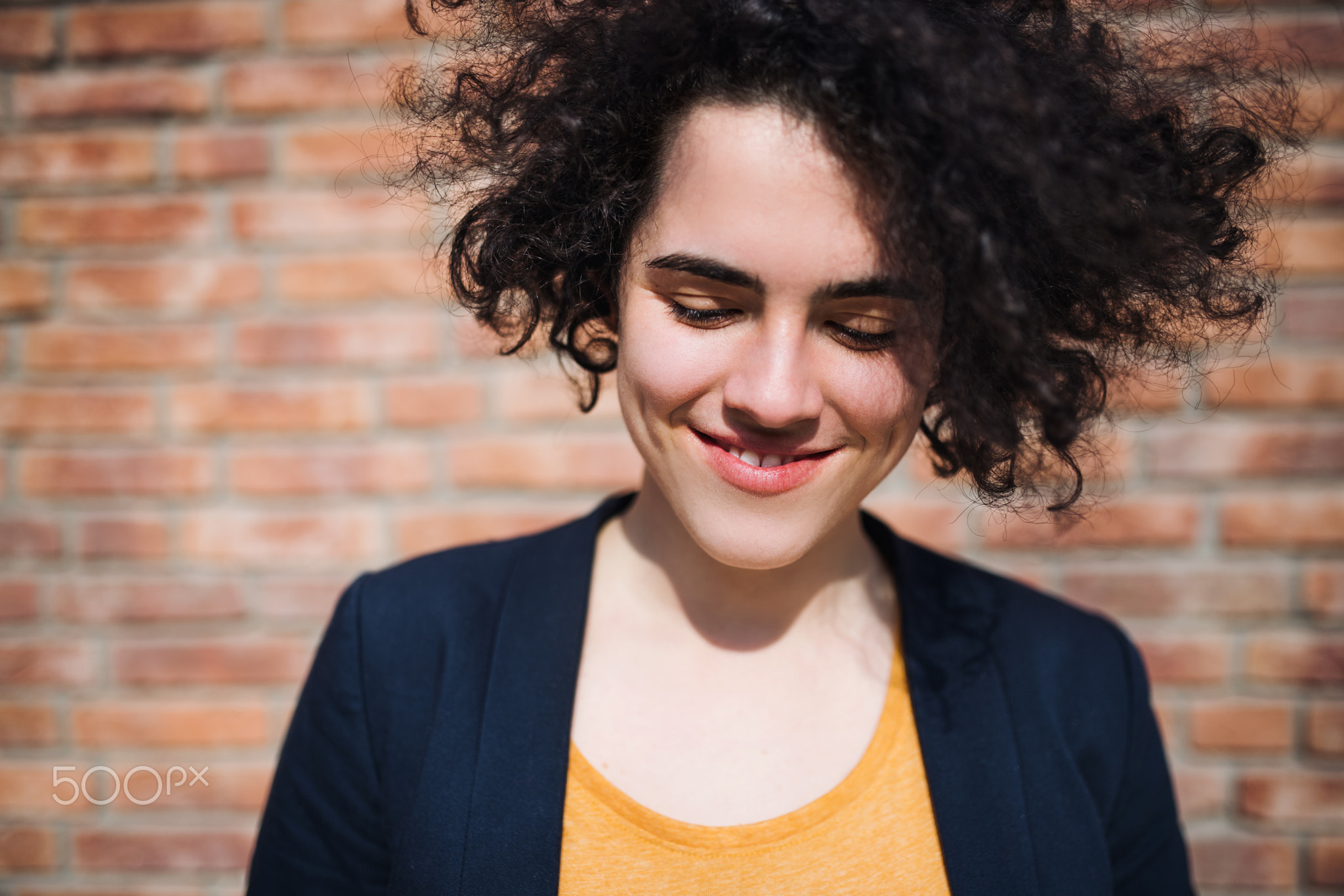 A happy young business woman standing outdoors, brick wall in the background.