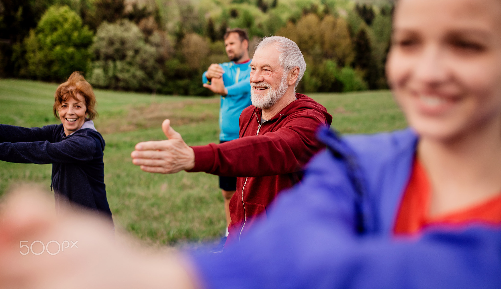 Large group of fit and active people doing exercise in nature, stretching.