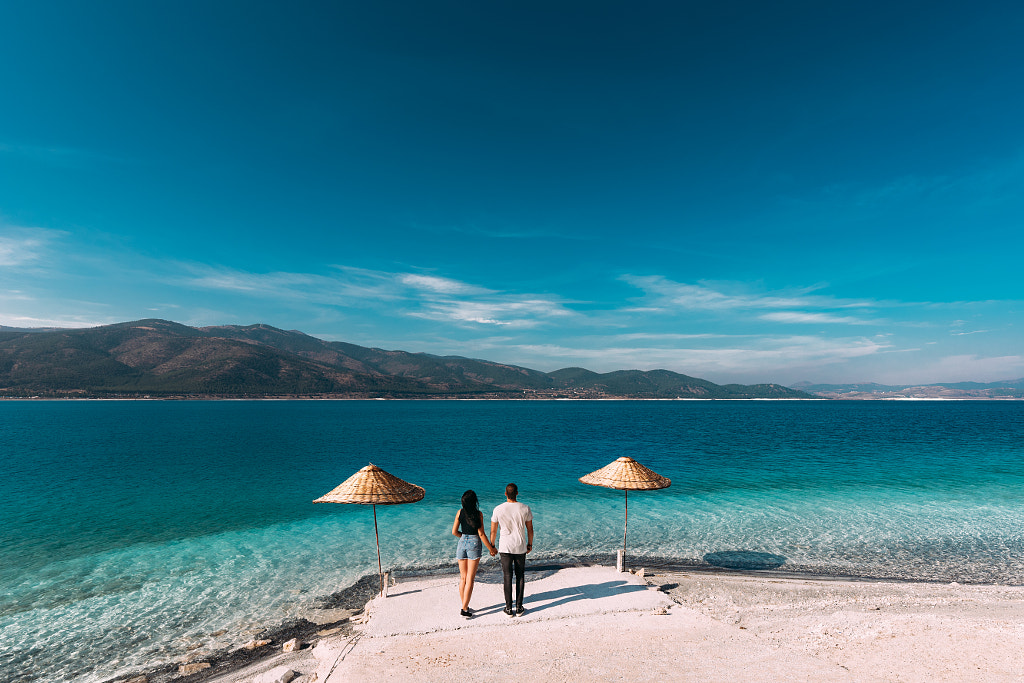 Couple poses - A couple in love looks at the blue lagoon. Couple in love on the beach. Honeymoon lovers. Man and... by MISHA SOTNIKOV on 500px.com