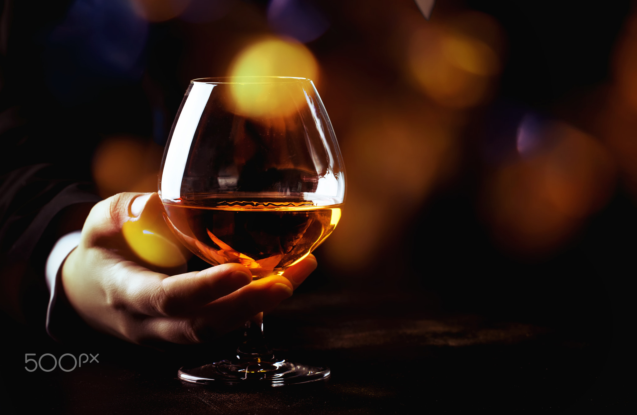 French glowing cognac glass in hand on the dark bar counter back