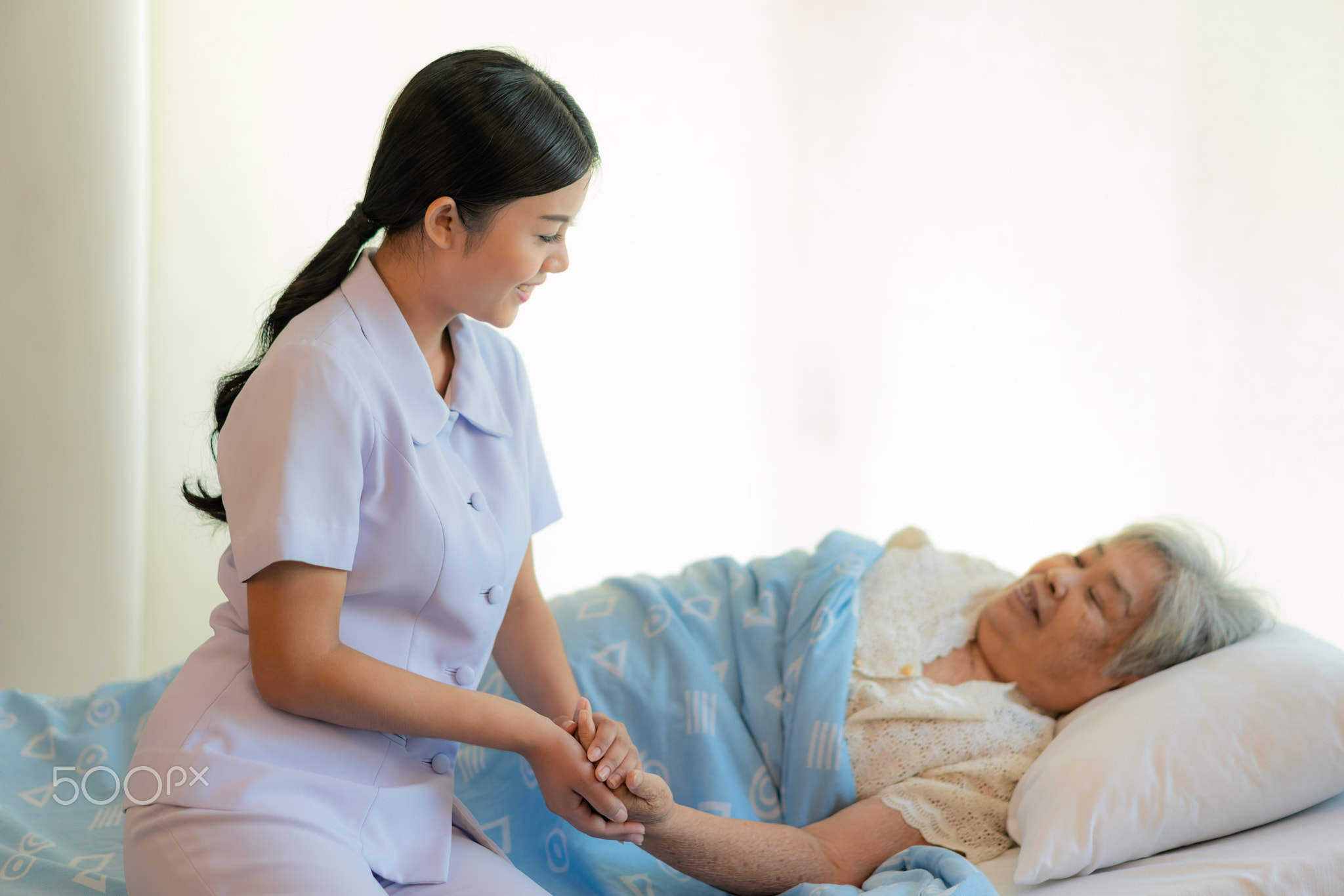 Nurse sitting on a hospital bed next to an older woman helping h