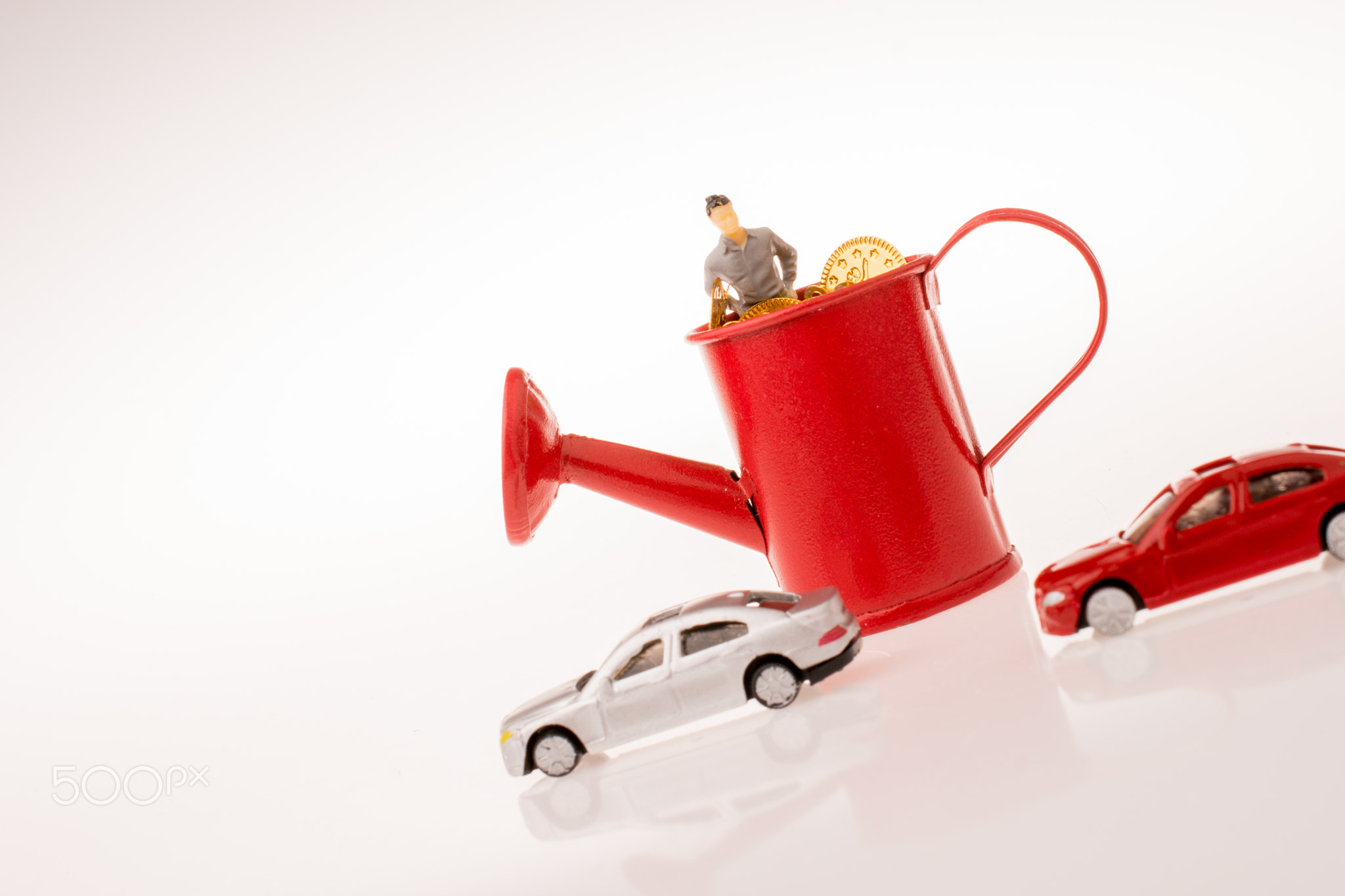 Figurine standing in a watering can with cars beside