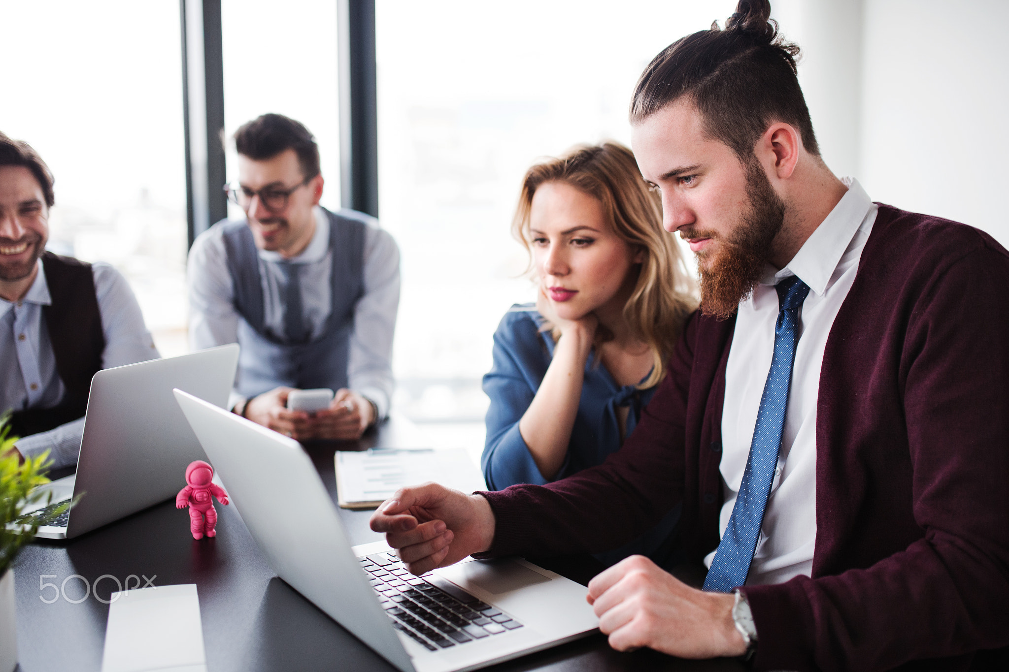 A group of young business people with laptop sitting in an office, talking.