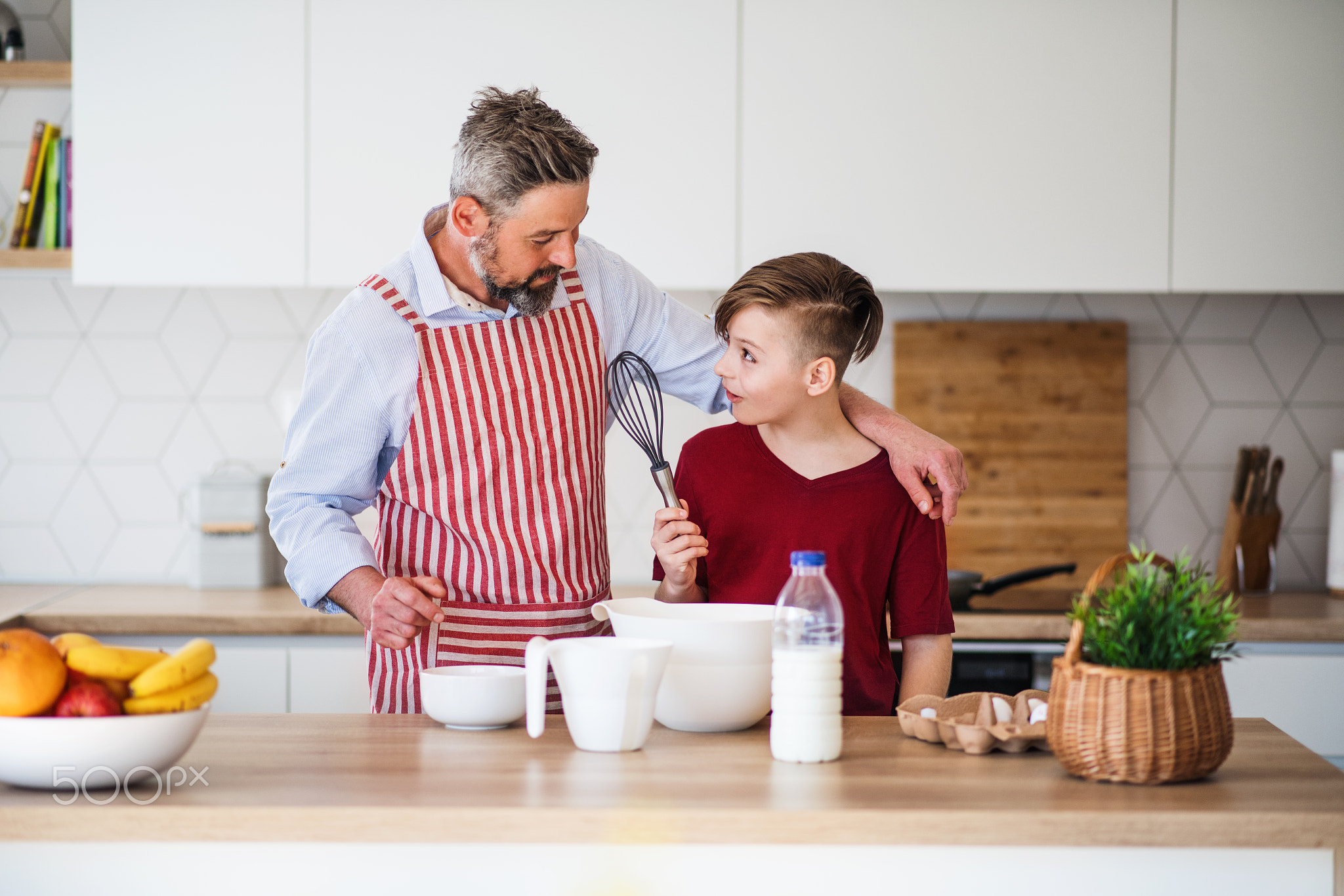 Mature father with small son indoors in kitchen, making pancakes.