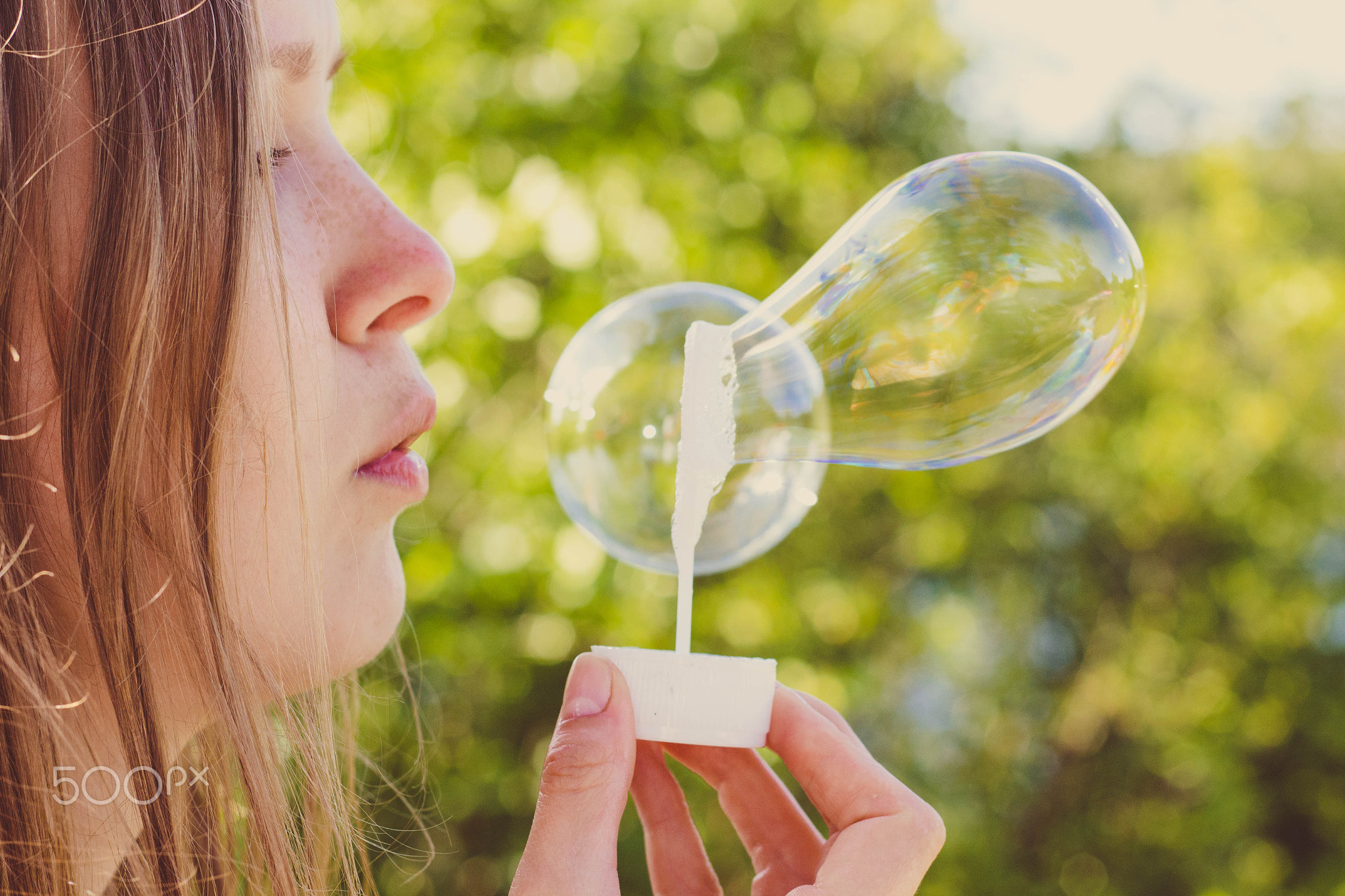 Beautiful and young girl blows soap bubbles