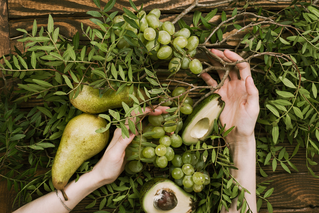 Flat lay of woman's hands holding grapes, pears and avocados with pistachio branches on wooden table by Nataly Lavrenkova on 500px.com