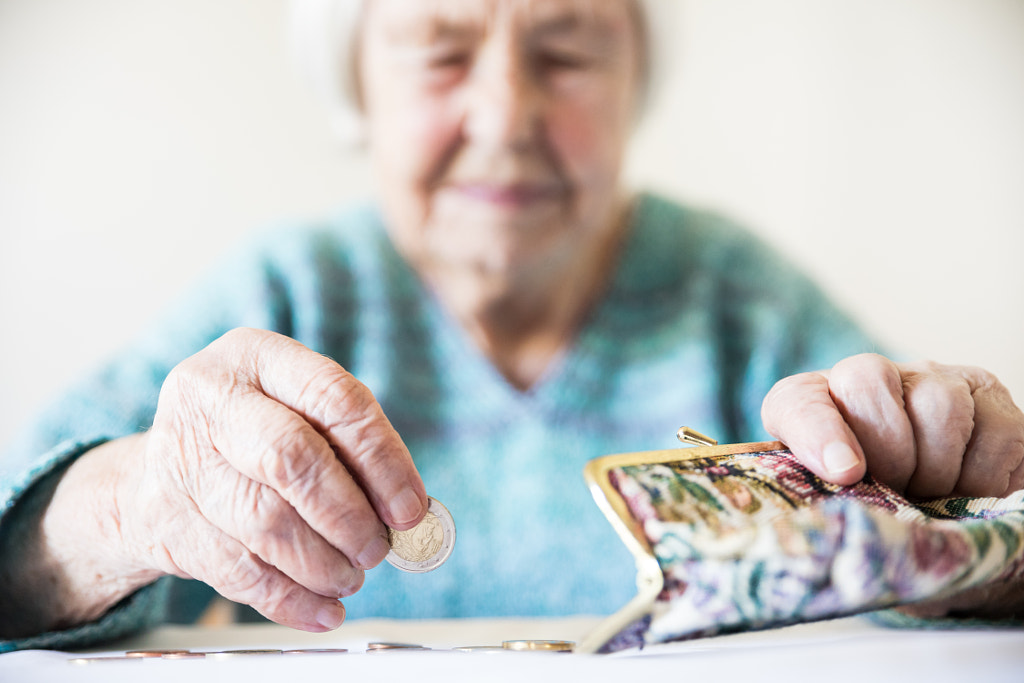 Concerned elderly woman sitting at the table counting money in her wallet. by Matej Kastelic on 500px.com