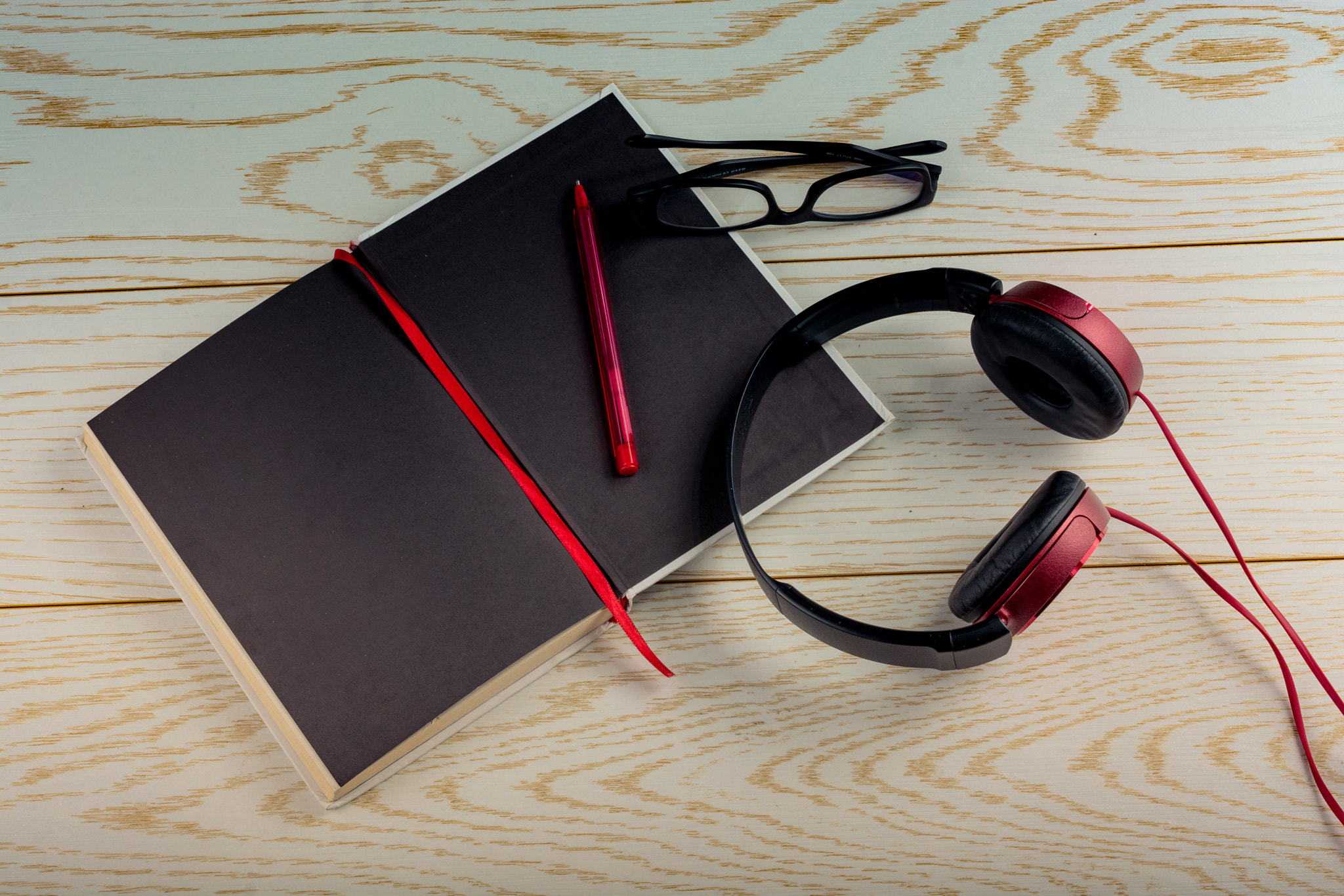 Headphones, notebook, pen and glasses on wooden background