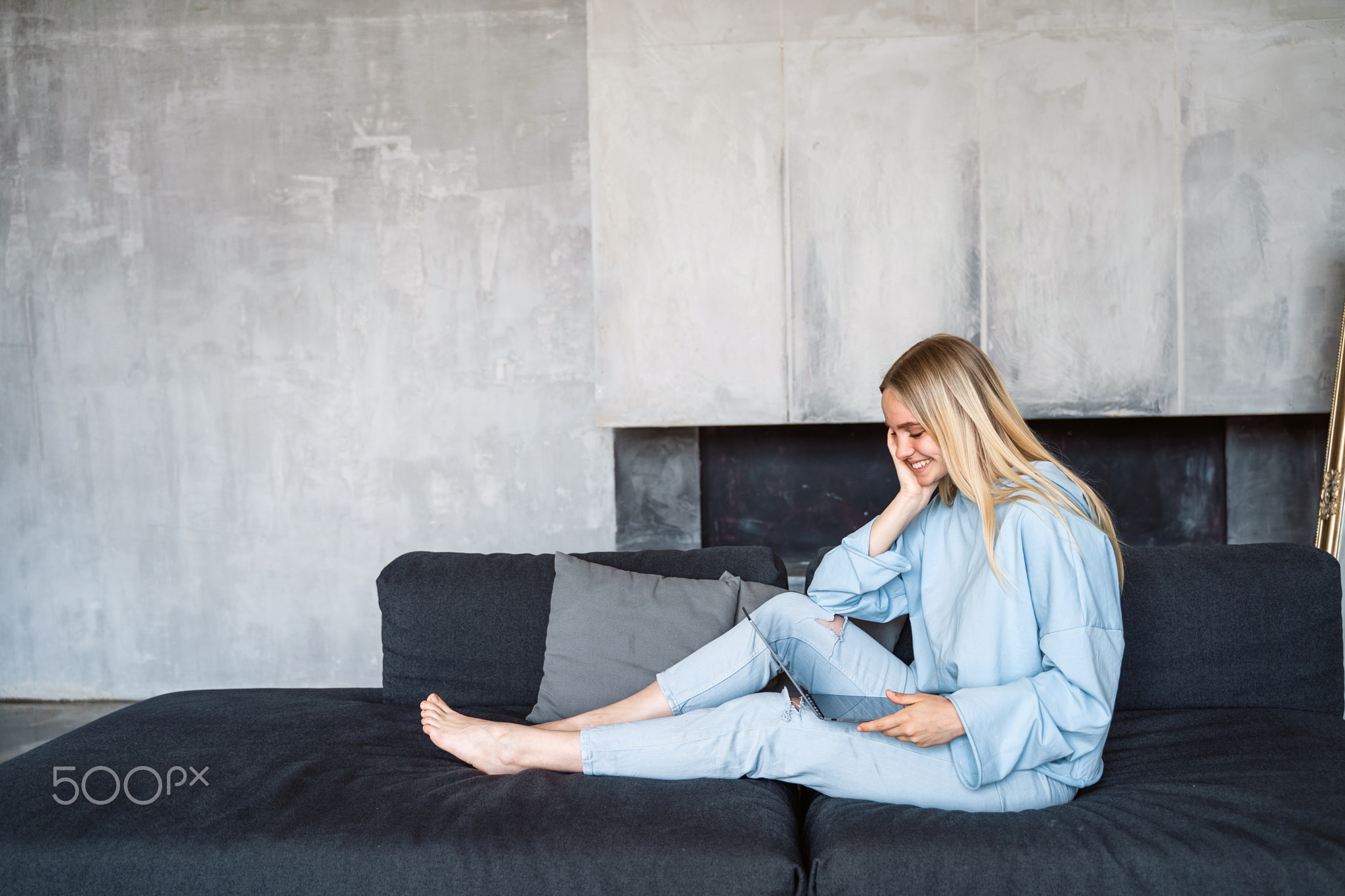 Image of happy woman using silver laptop while sitting on sofa