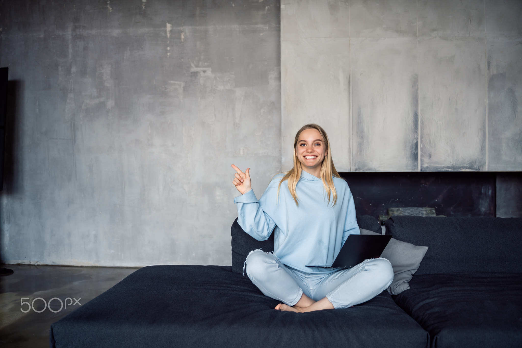 Image of happy woman using silver laptop while sitting on sofa