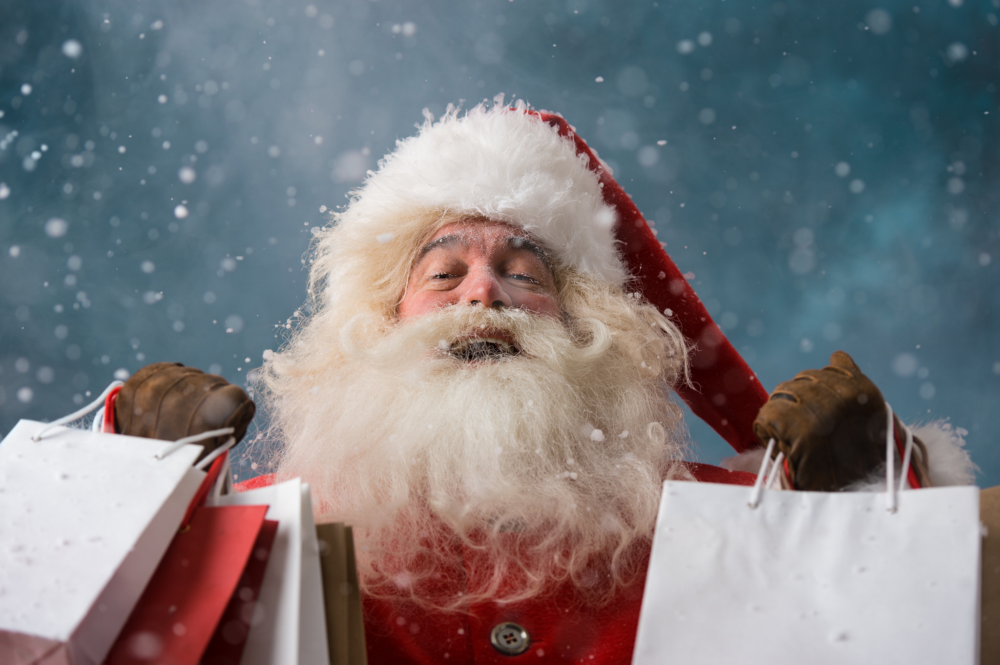 Santa Claus outdoors in snowfall holding shopping bags