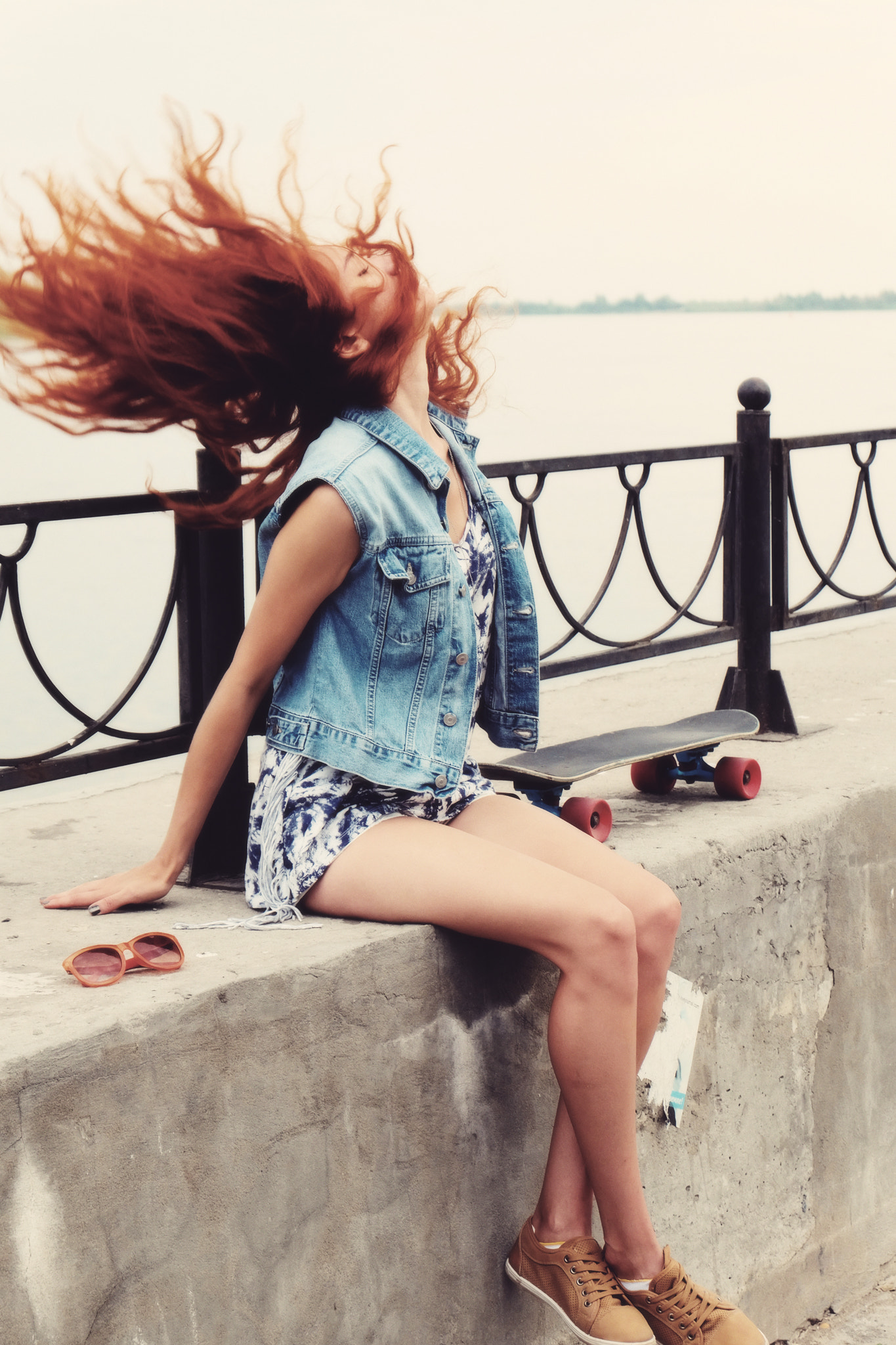 Toned image of young women sitting with skateboard on parapet and shake her hair