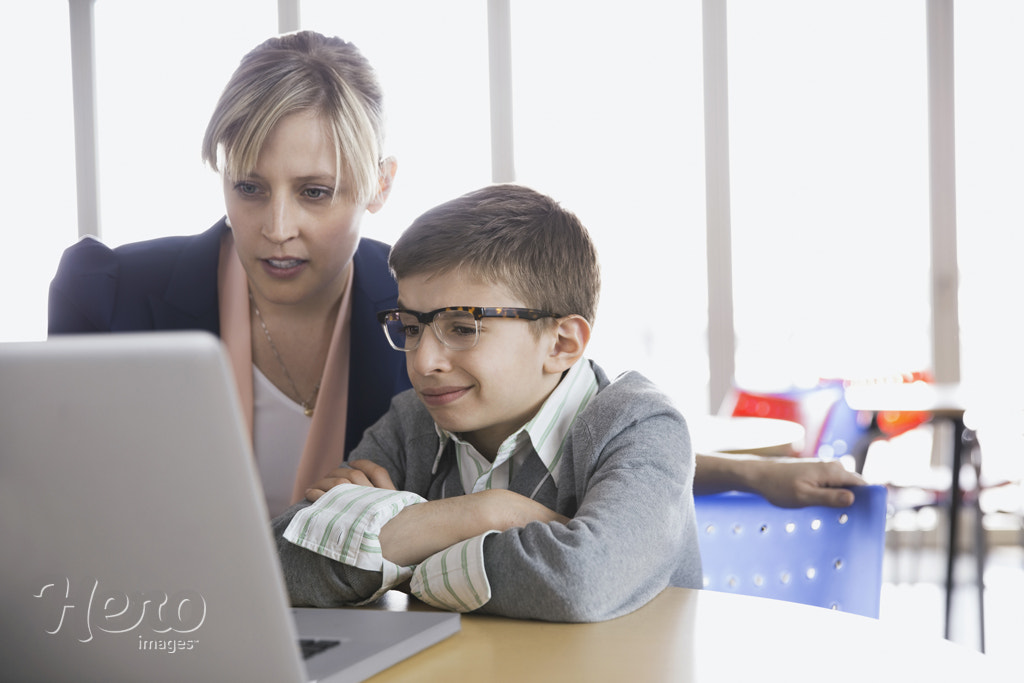 School boy and teacher using laptop in classroom