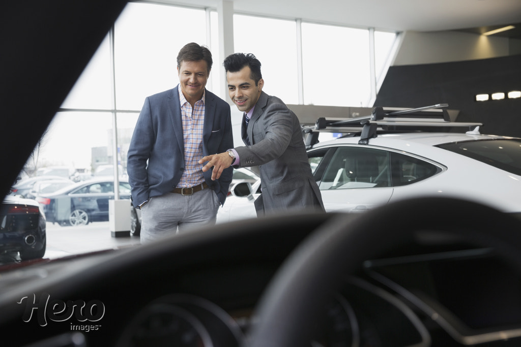 Salesman talking to man in car dealership showroom