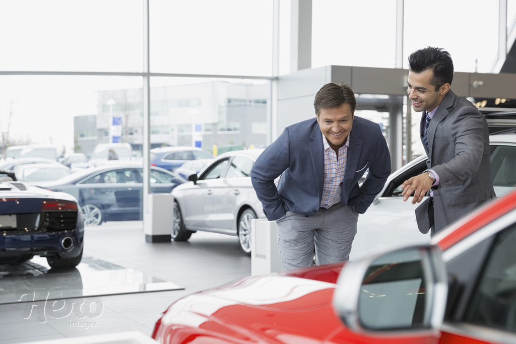 Salesman showing man car in dealership showroom