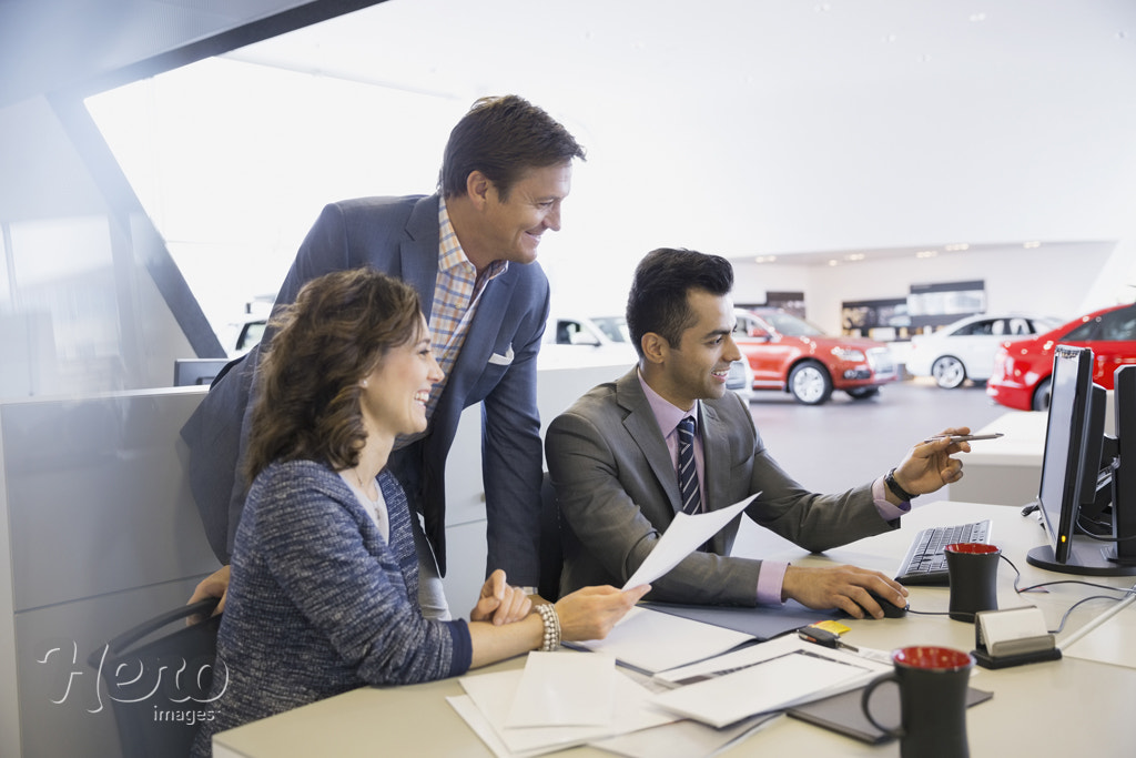 Salesman and couple finalizing paperwork in car dealership