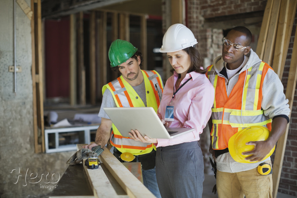 Female architect discussing plans on laptop with tradesmen at construction site