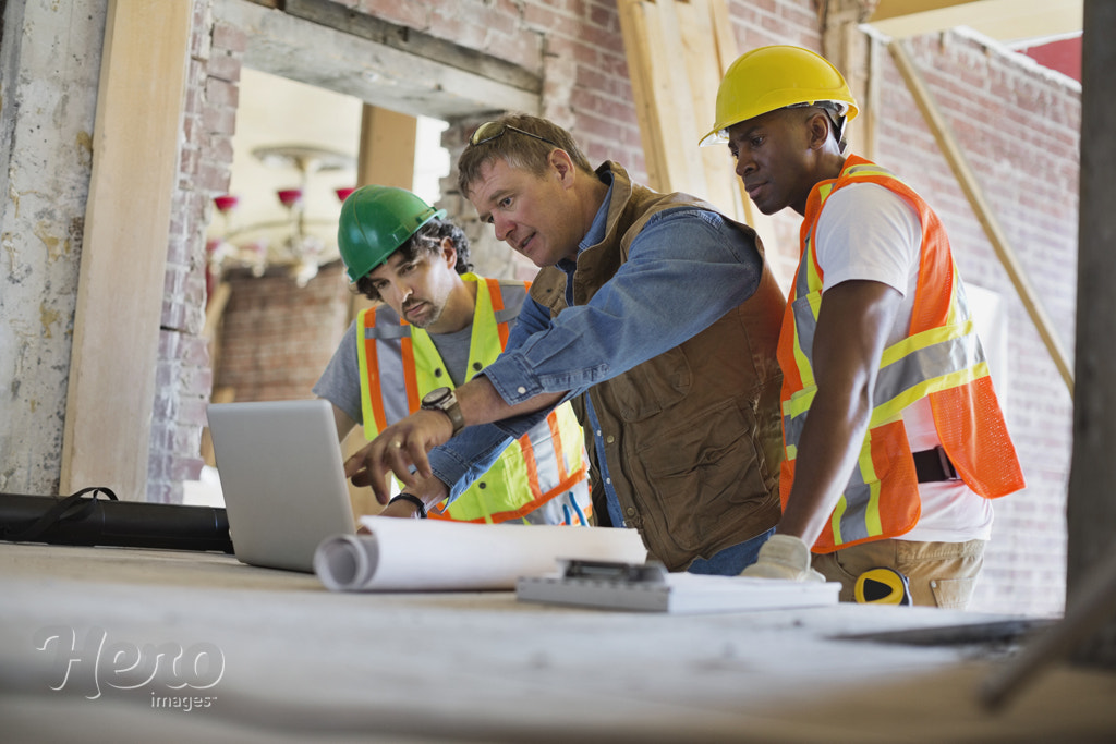 Foreman discussing plan on laptop with tradesmen at construction site