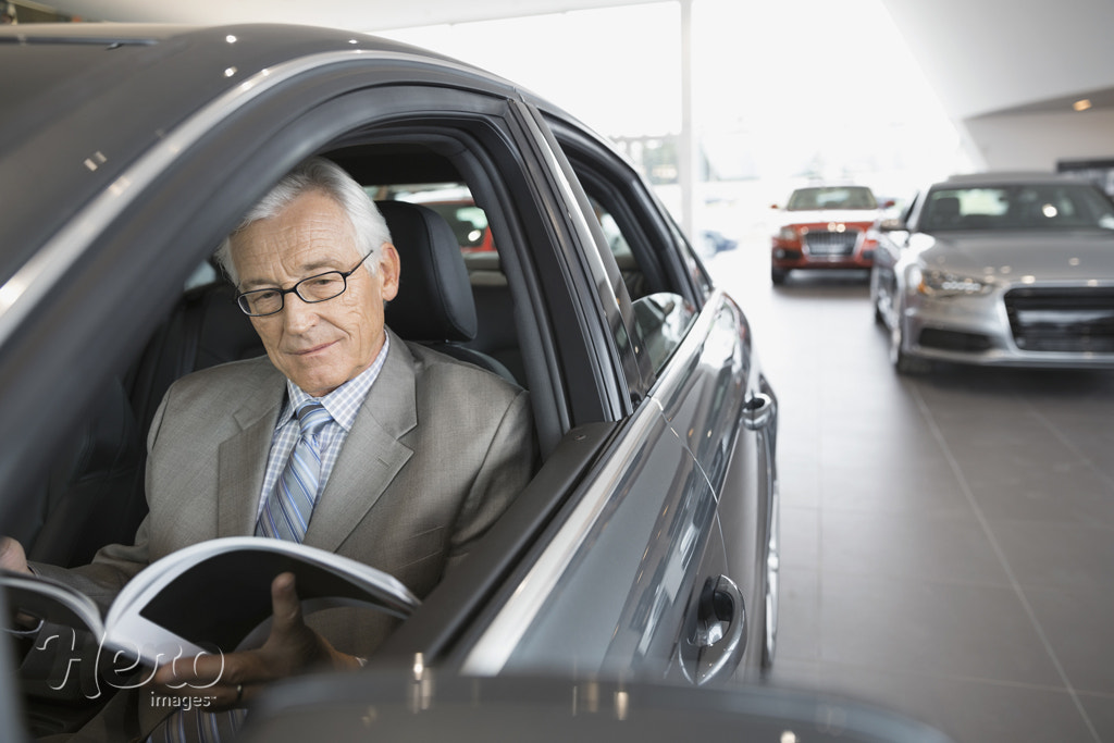 Man with brochure inside car in dealership showroom