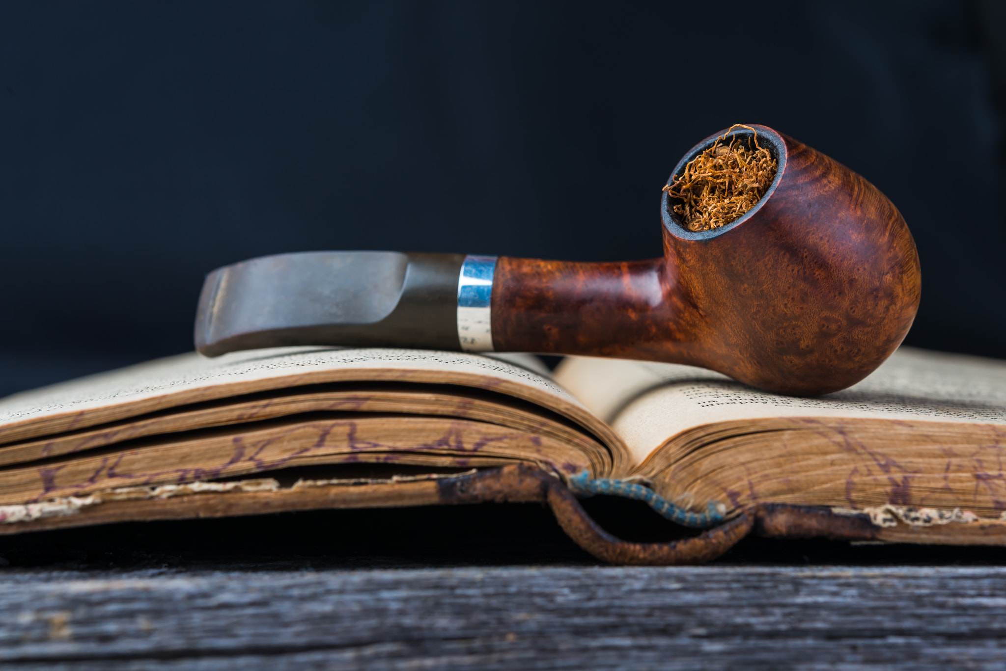 smoking pipe on the opened old book in wooden grey table.