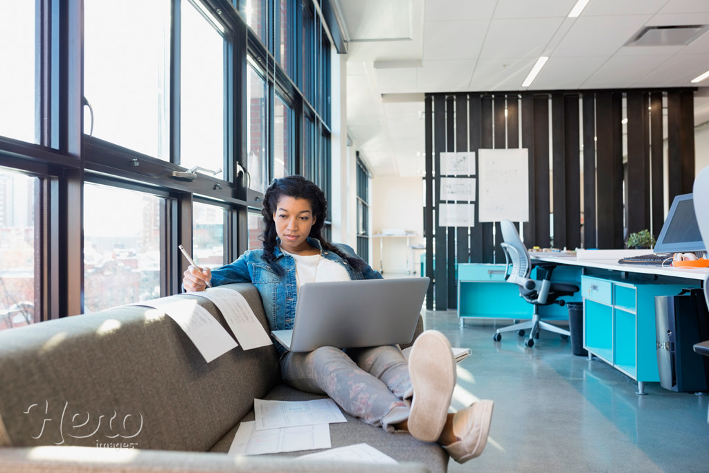 Designer working at laptop on sofa in office